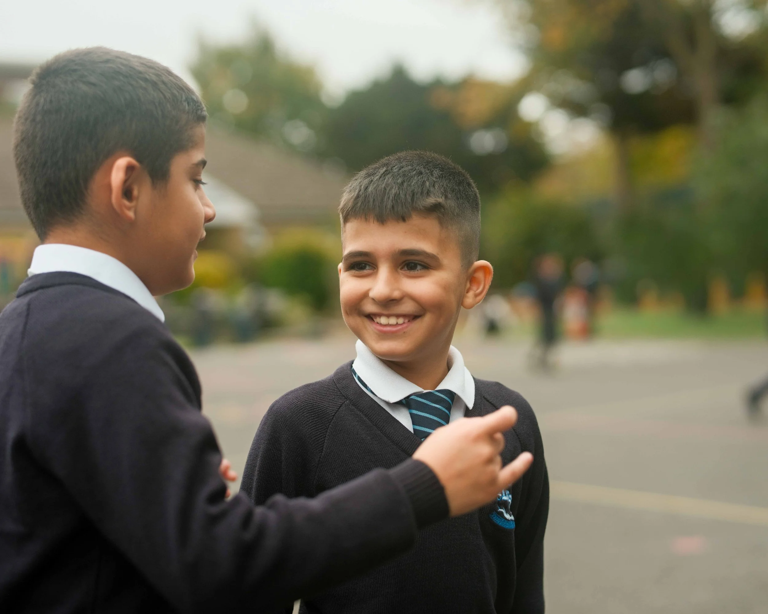 Two schoolboys in uniforms talking outdoors.