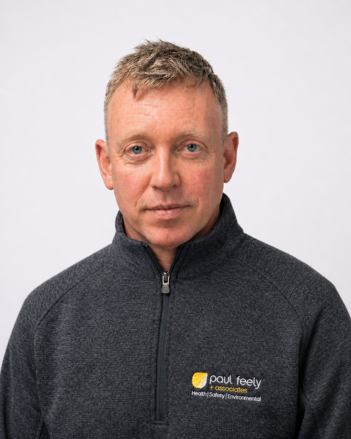 Portrait of a man with short blonde hair, wearing a dark gray fleece jacket with a Paul Feely + Associates logo, standing against a plain white background.