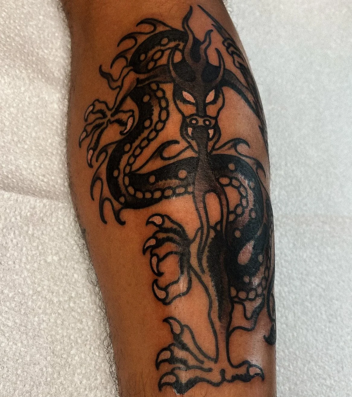 Black line tattoo of a dragon on a person's arm.