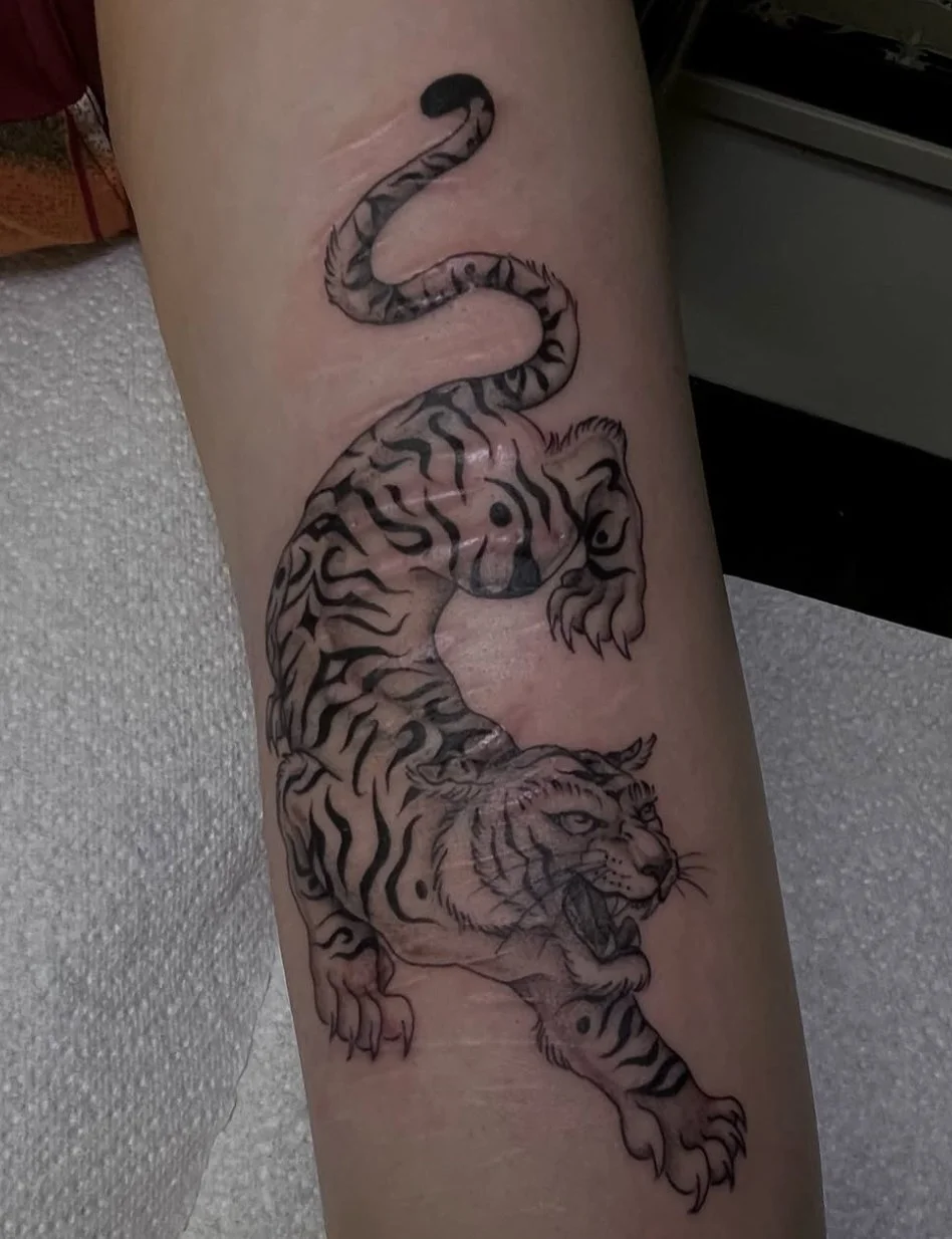 Tattoo of a tiger with a curled tail on a person's thigh.