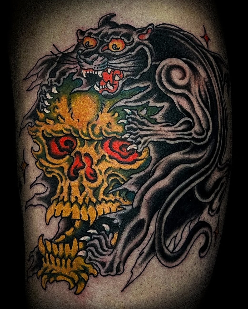 Tattoo of a black panther intertwined with a yellow and red flaming skull on skin.