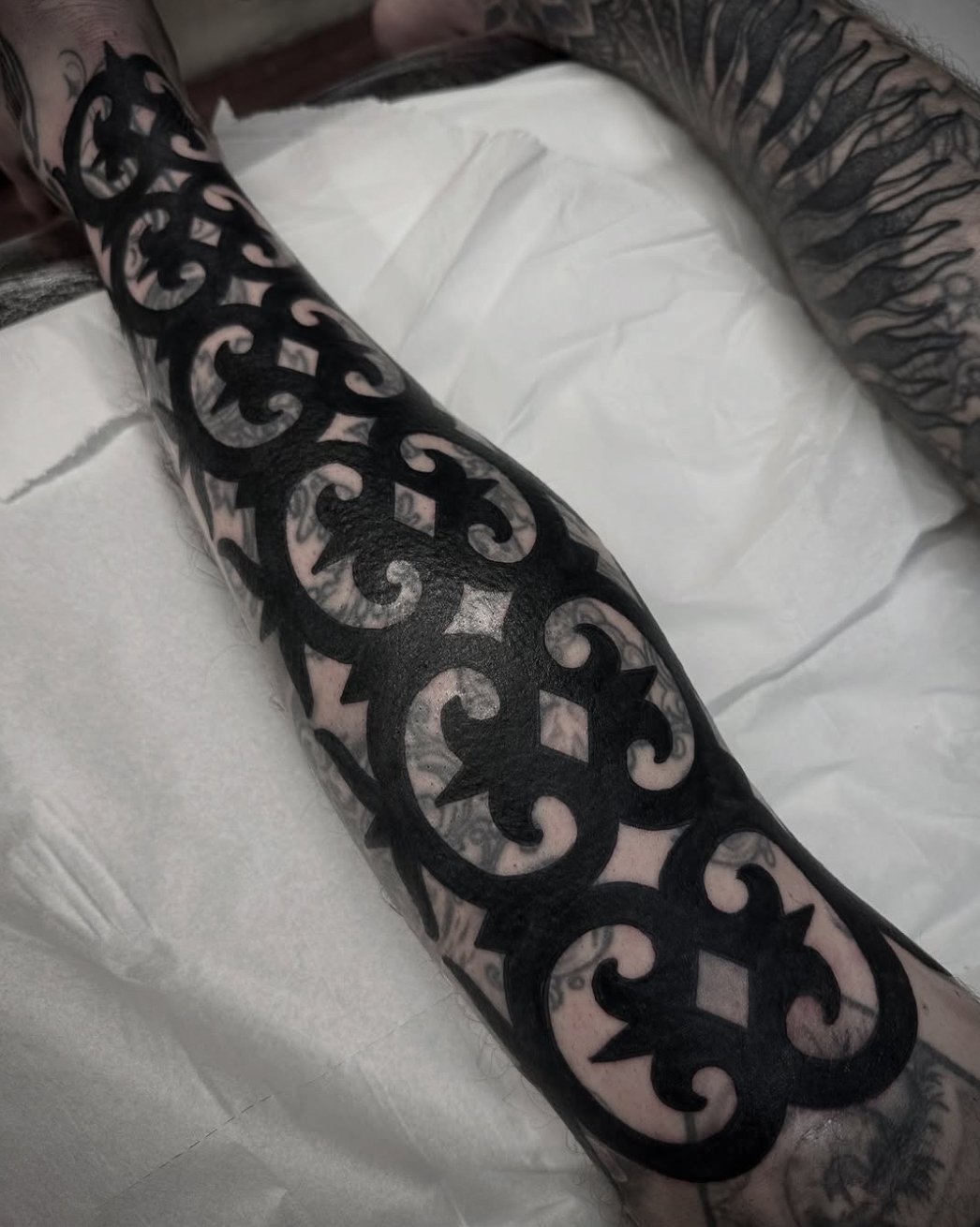 A person's arm with a large black tattoo featuring intricate scrollwork and geometric patterns.