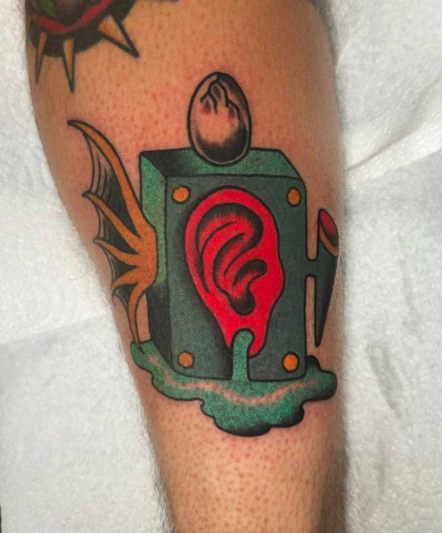 Tattoo of a speaker with a red ear and green slime, with additional details and parts visible.