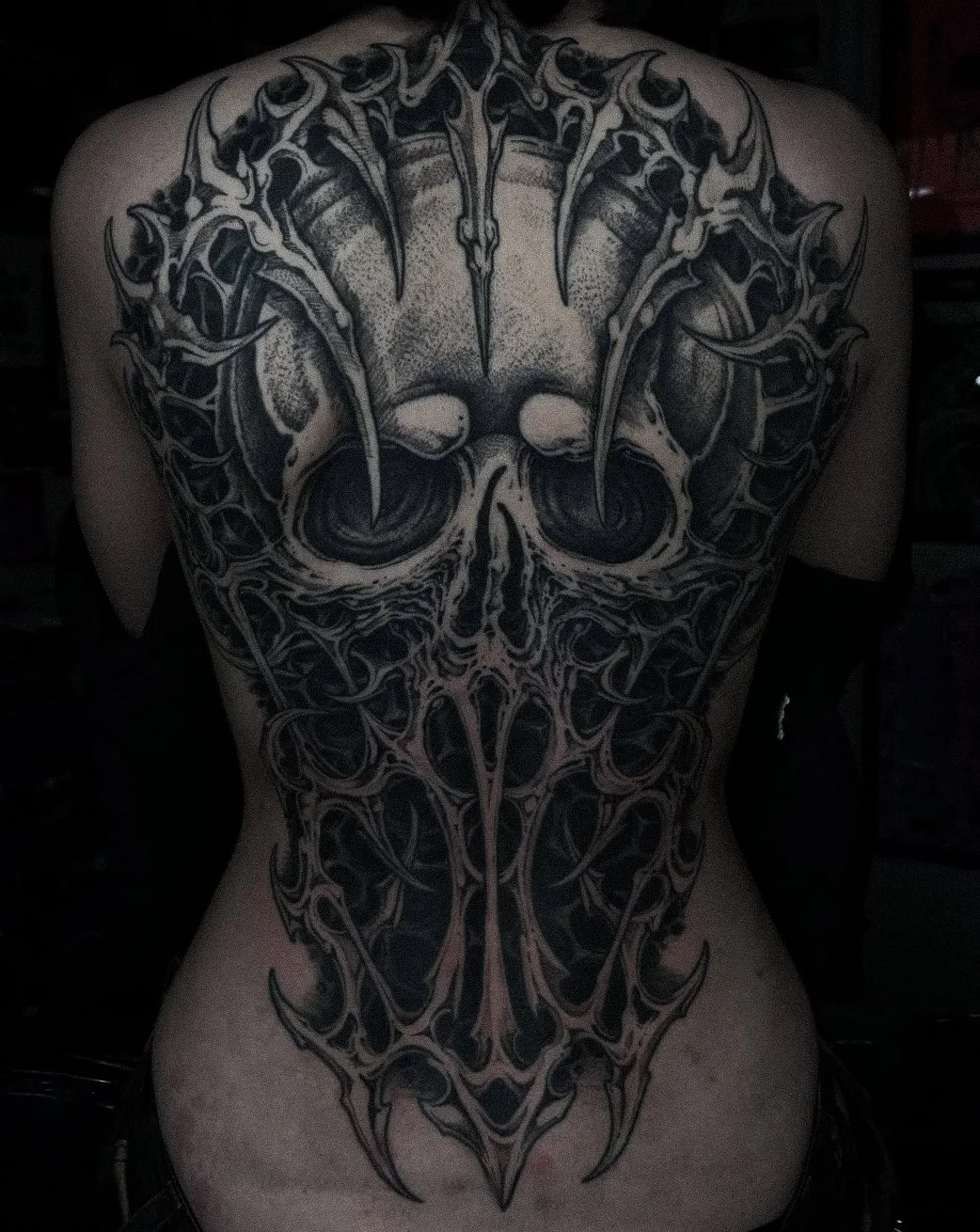 Detailed black and gray tattoo on a person's back featuring a stylized skull with intricate patterns and sharp elements.