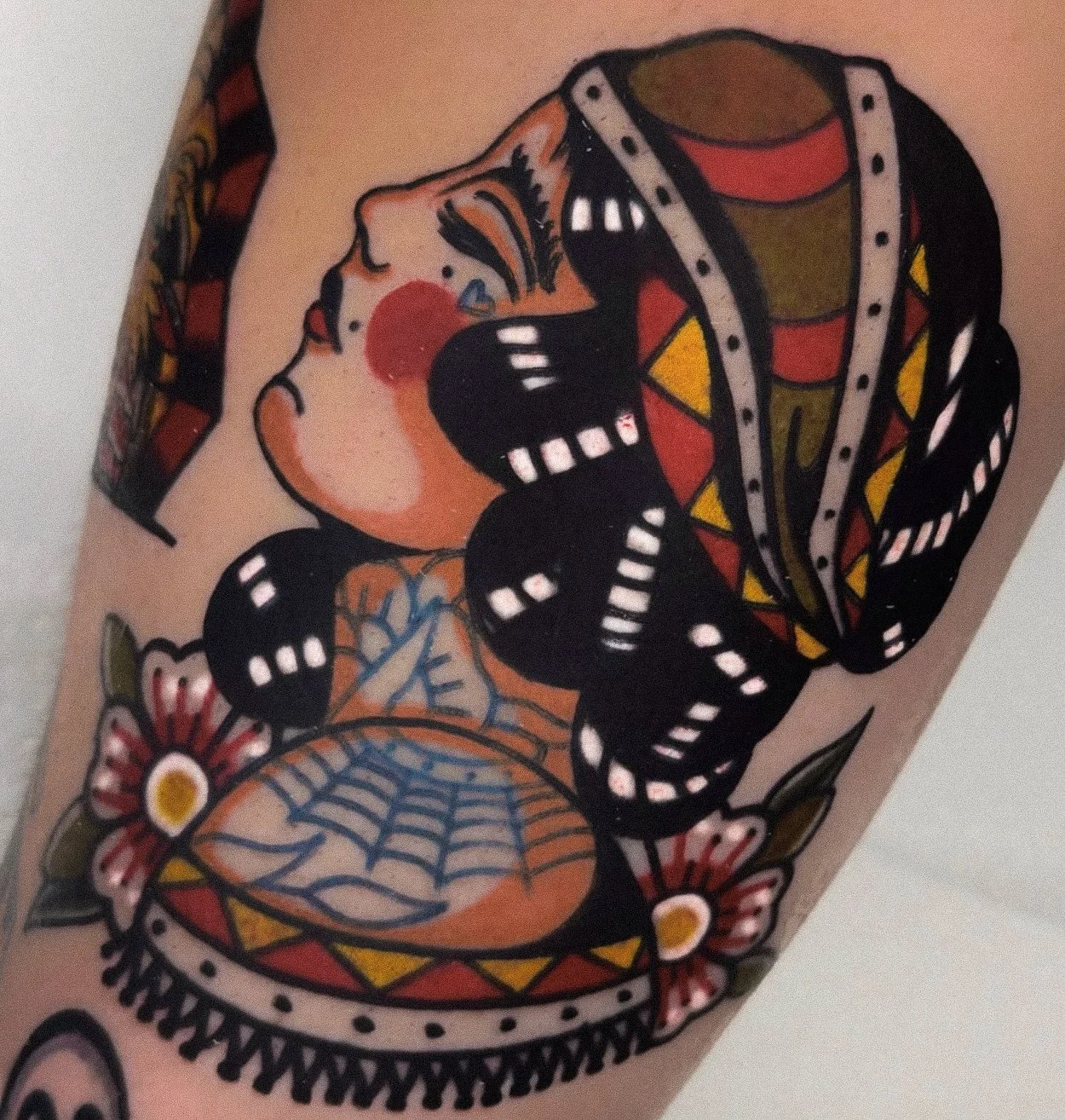 Tattoo of a woman with closed eyes, red cheeks, and long dark hair, surrounded by a black butterfly with white markings and pink flowers with yellow centers.