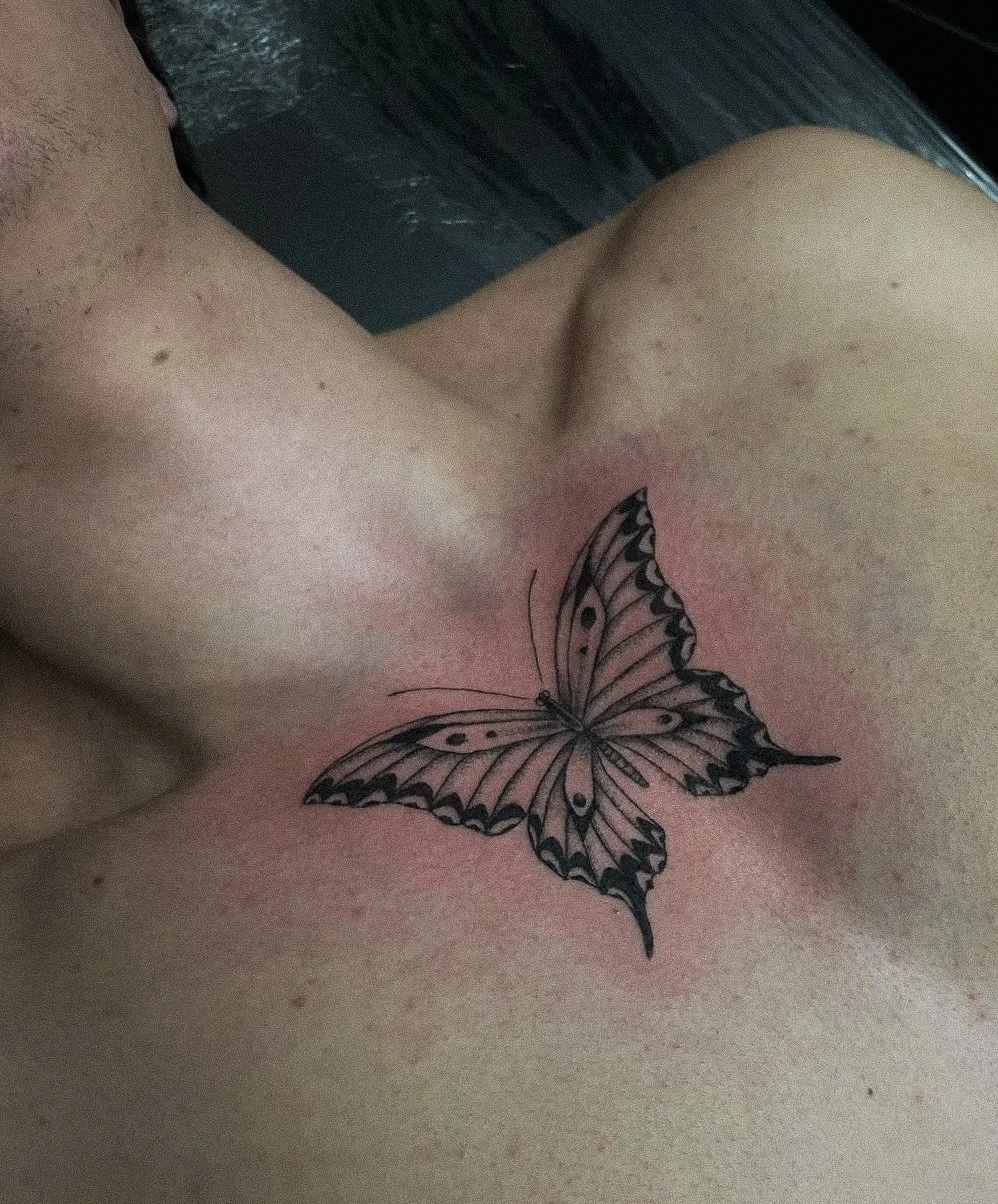 A black and gray butterfly tattoo on a person's shoulder and chest area.