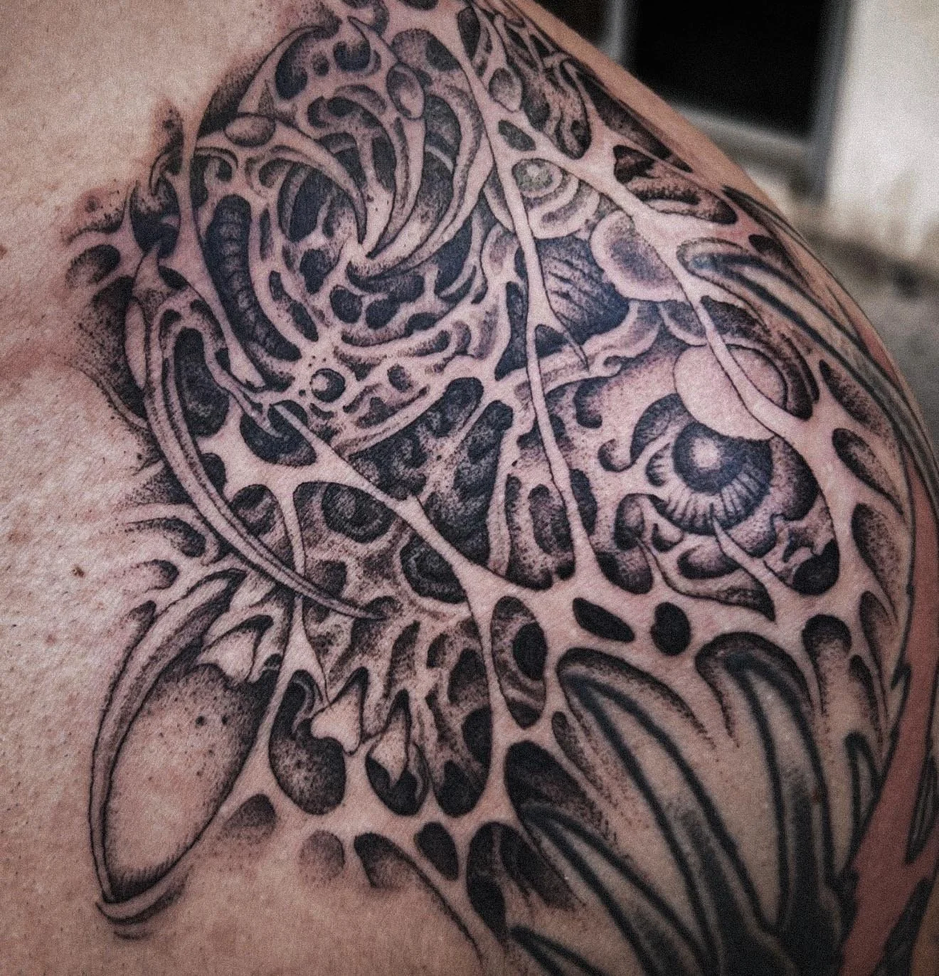 Close-up of a black and gray tattoo of a butterfly with detailed patterns on a person's shoulder.