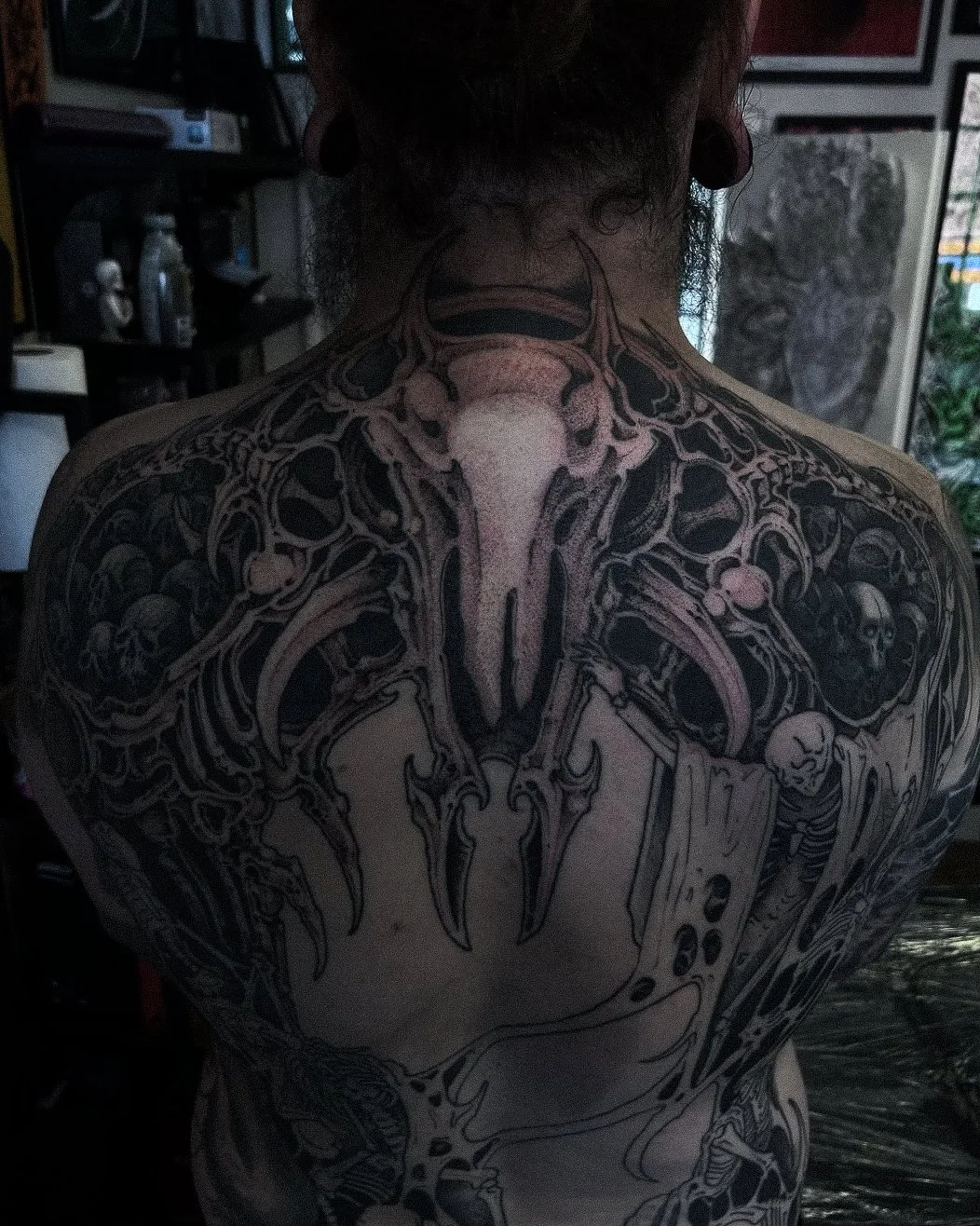 Back of a person with a detailed black and gray skull tattoo covering the upper back and shoulders.