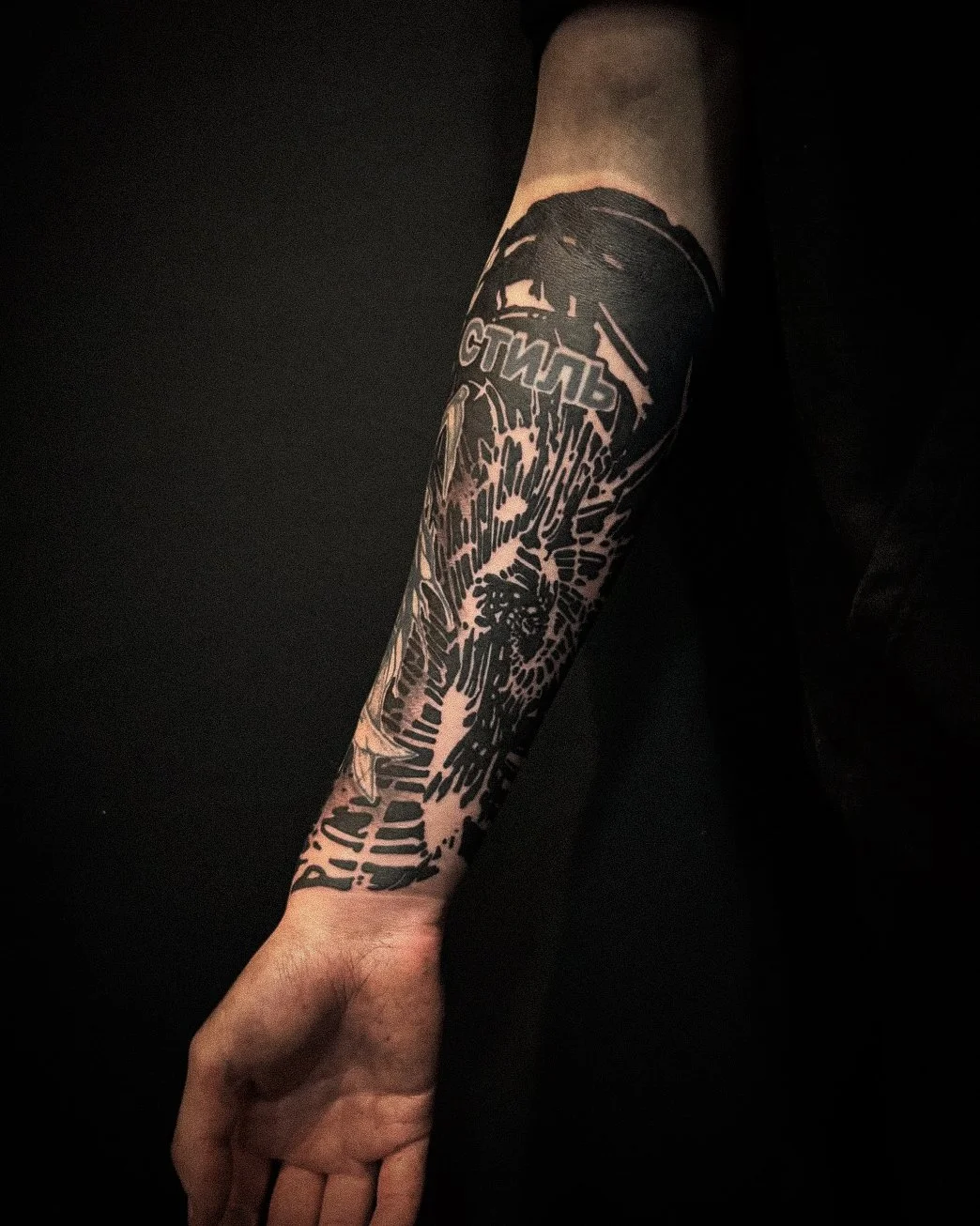 Black and white tattoo of a person's arm featuring a stylized face, text, and patterns.