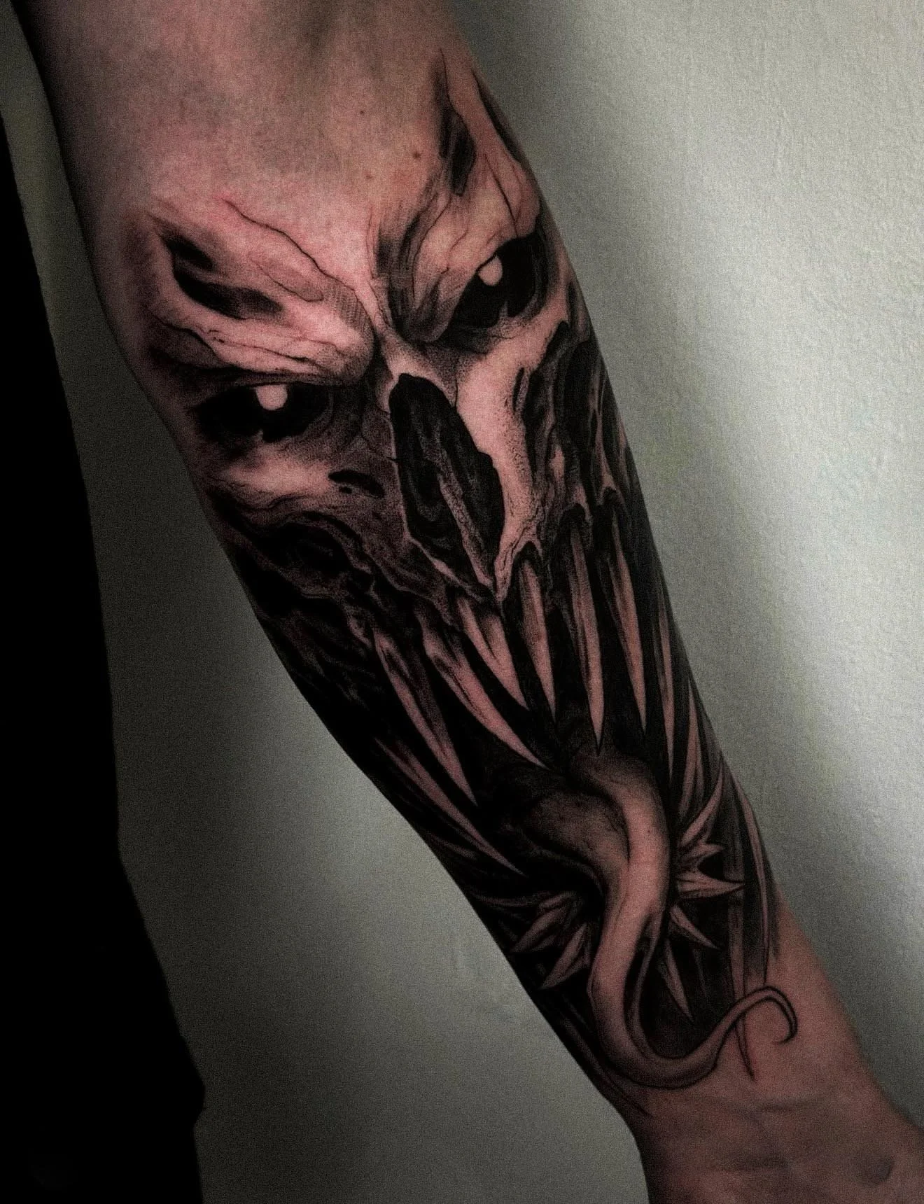 Black and gray detailed tattoo of a clown face with dark eyes and a sinister expression, combined with a snake intertwined with the design on the forearm.