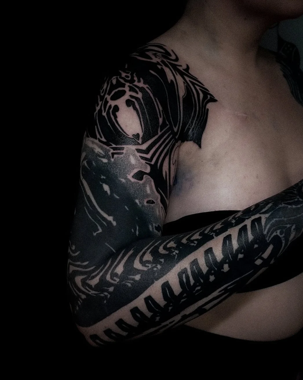 A person's shoulder and arm with black and grey tattoo artwork.