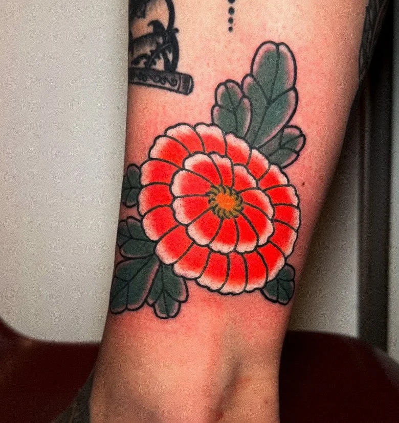 A vibrant traditional style tattoo of a red and white flower with green leaves on a person's arm.