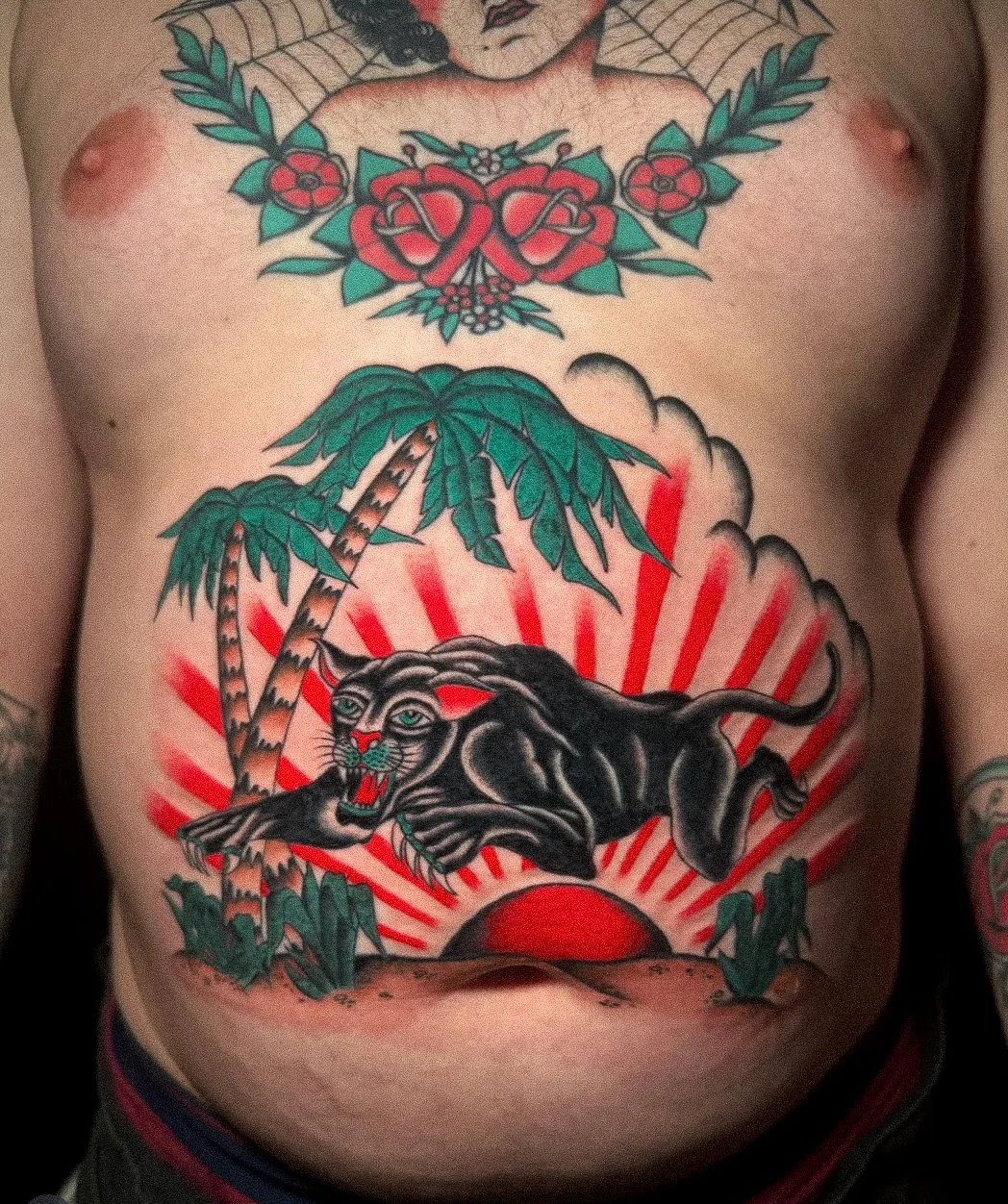 Colorful tattoo on person's chest depicting a black panther with blue eyes and red tongue, a palm tree, a sunrise, and stylized leaves.