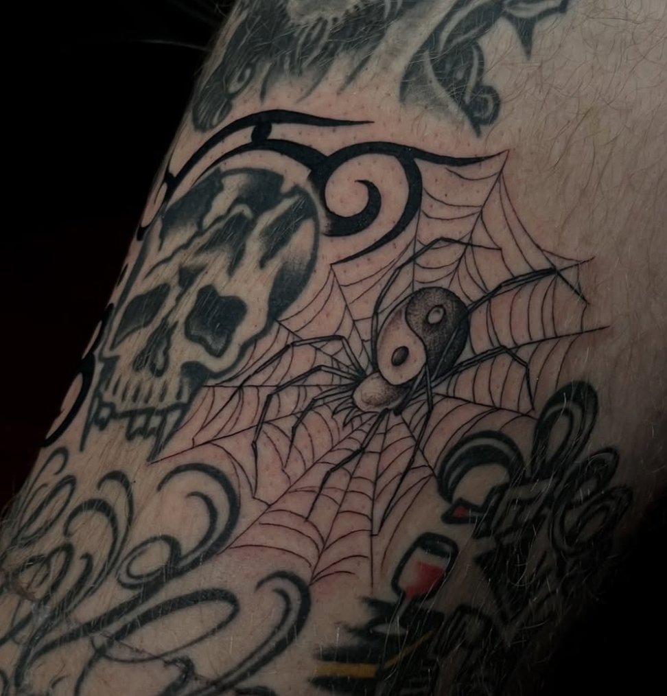 Tattoo of a spider on a web, a skull, and a yin-yang symbol.