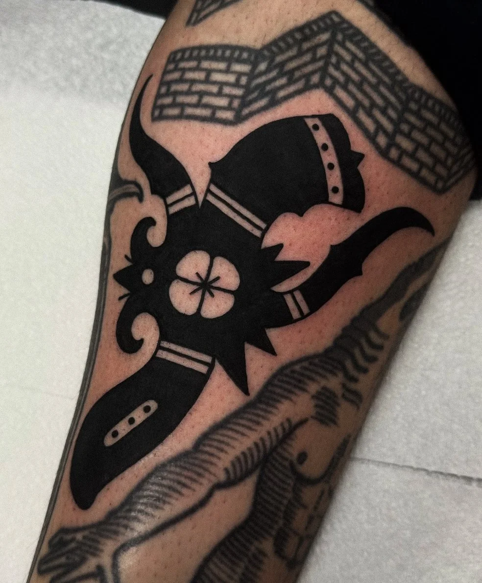 Tattoo of a black bat with a flower in its mouth, surrounded by brick-patterned designs.