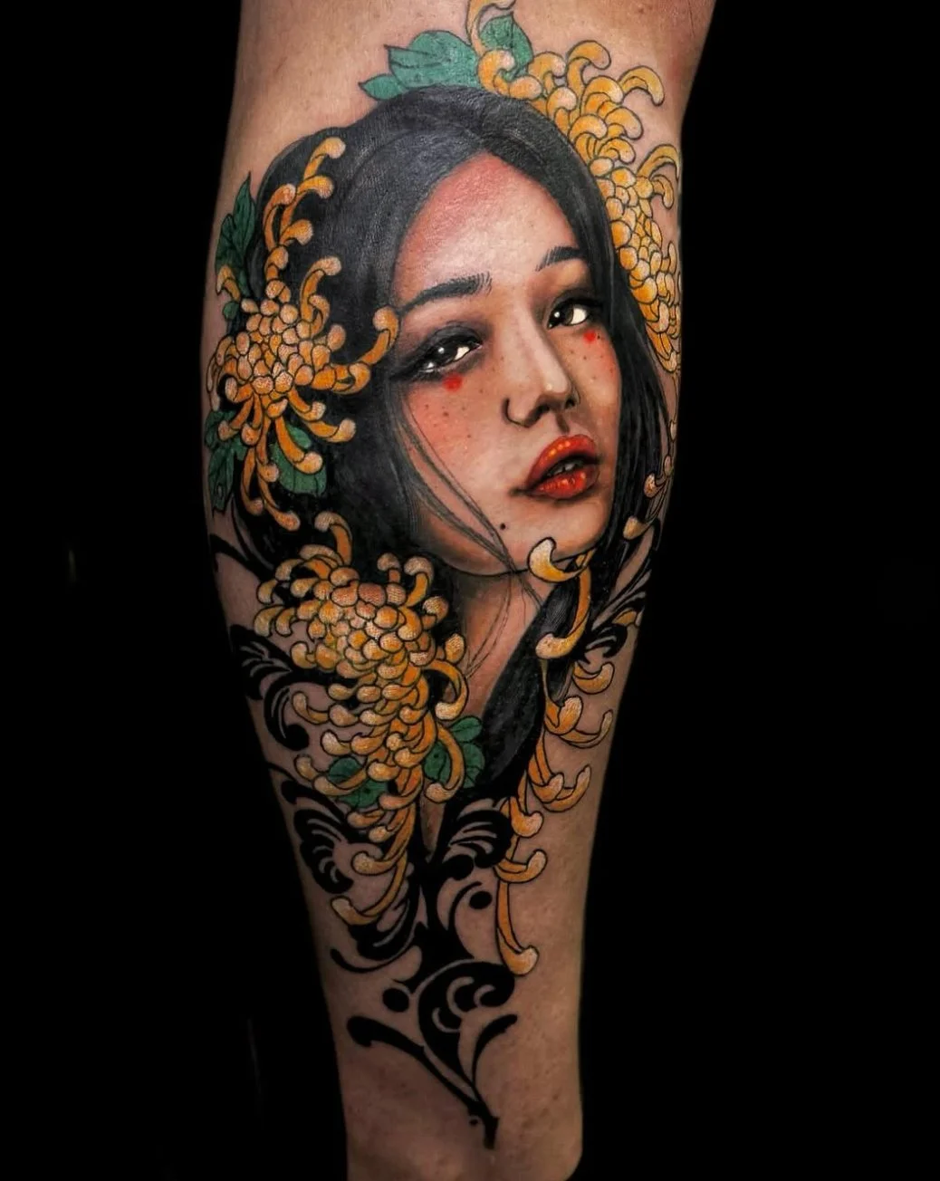 Tattoo of a woman's face with black hair, orange flowers, and green leaves surrounding her head on the arm.