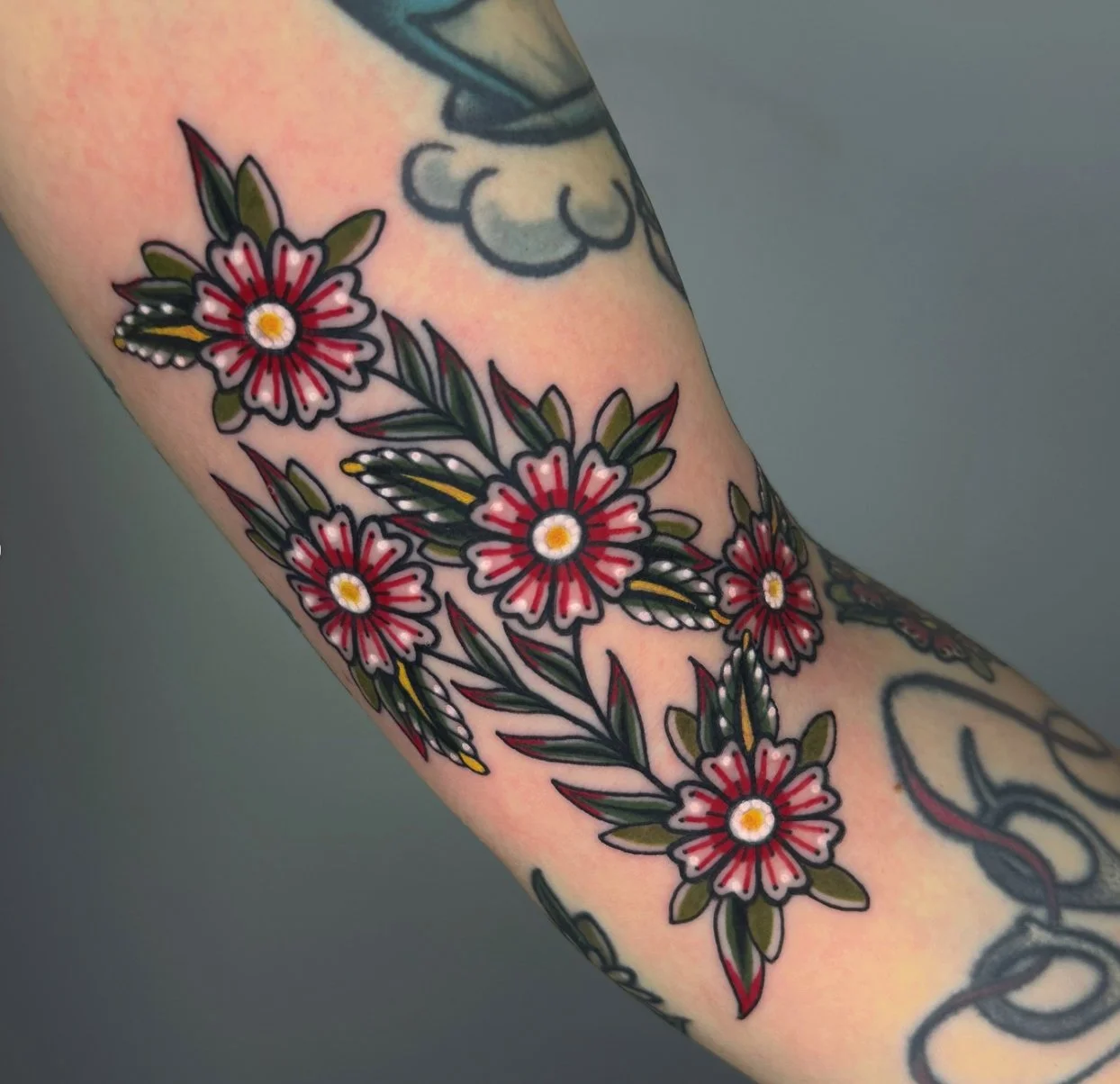 Tattoo of red, pink, and white flowers with green leaves on a person's arm.
