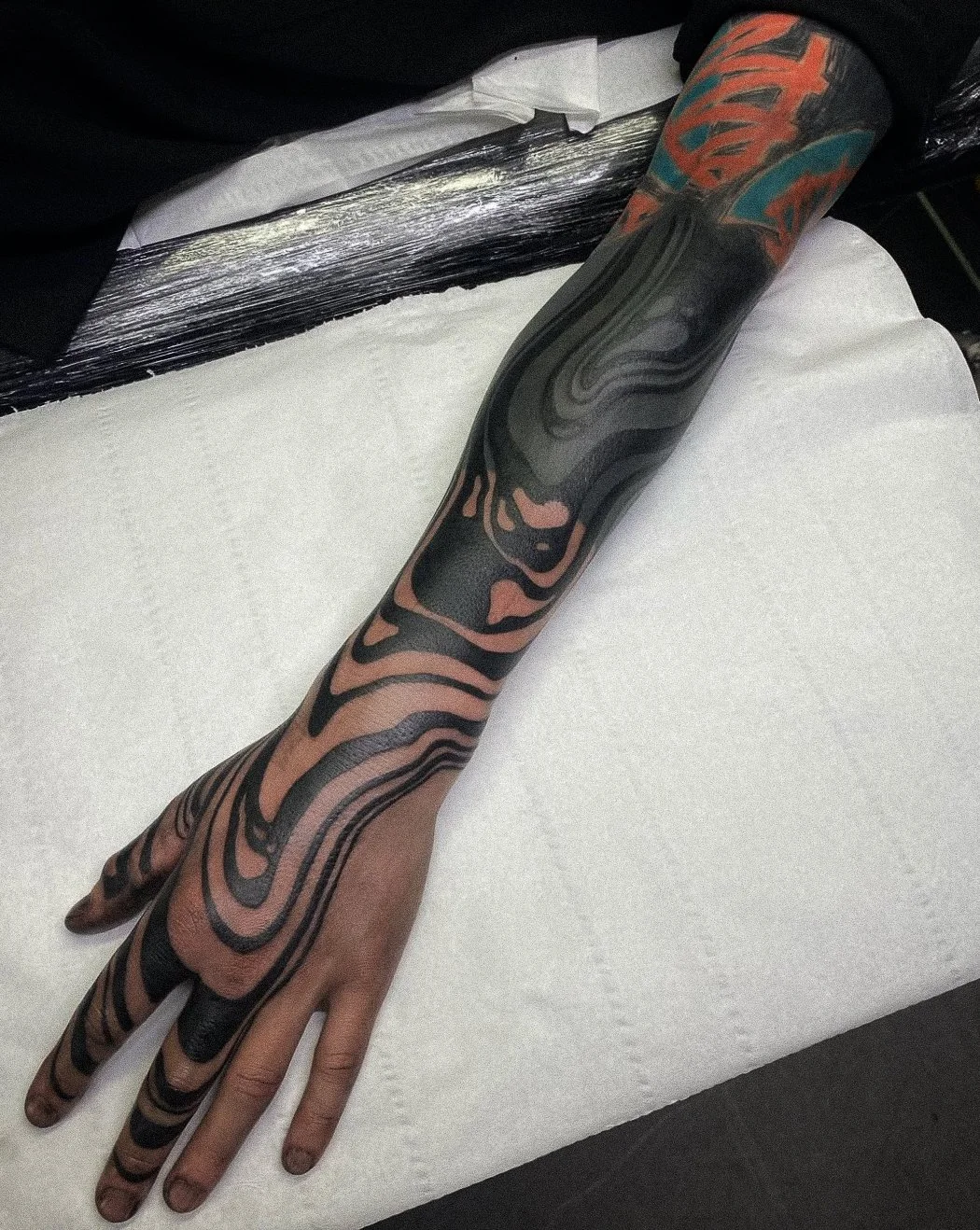 Tattooed arm with colorful and black abstract designs resting on white paper.