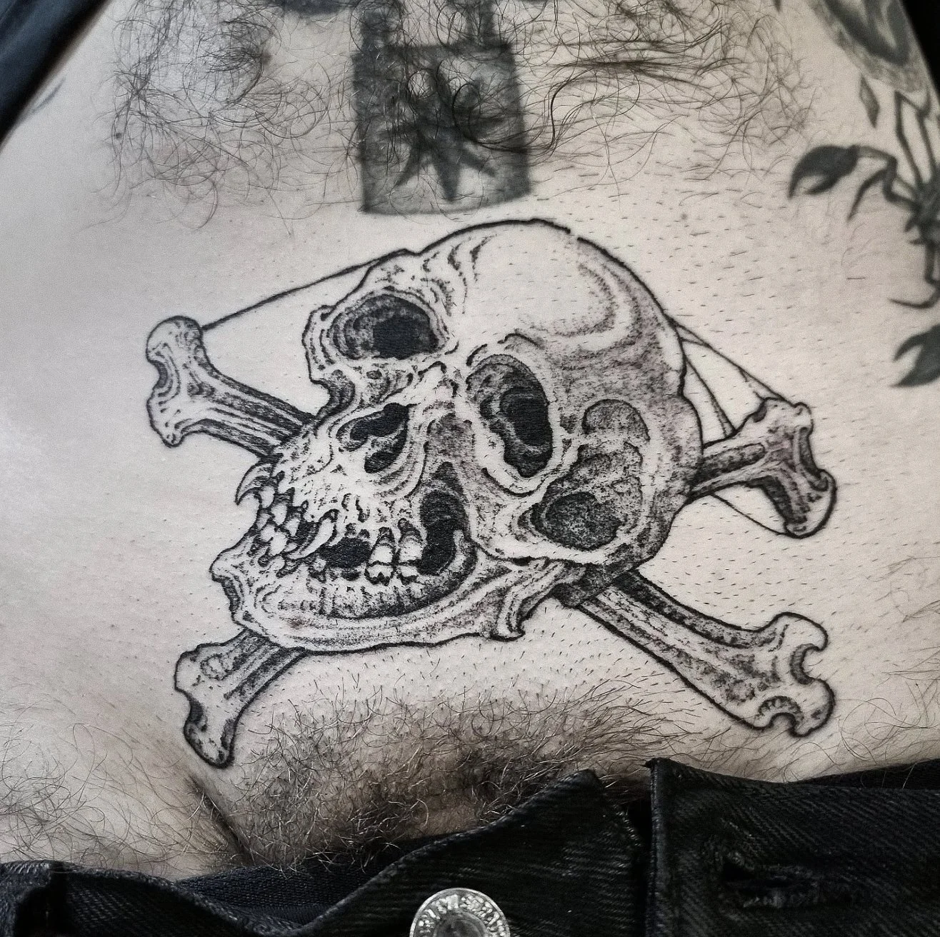 Tattoo of a skull and crossbones on a person's stomach, with hair and skin visible.
