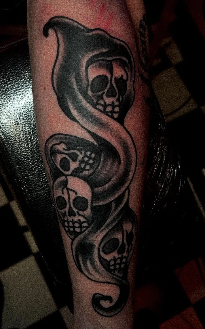 Tattoo of a snake intertwined with three skulls on a person's arm.