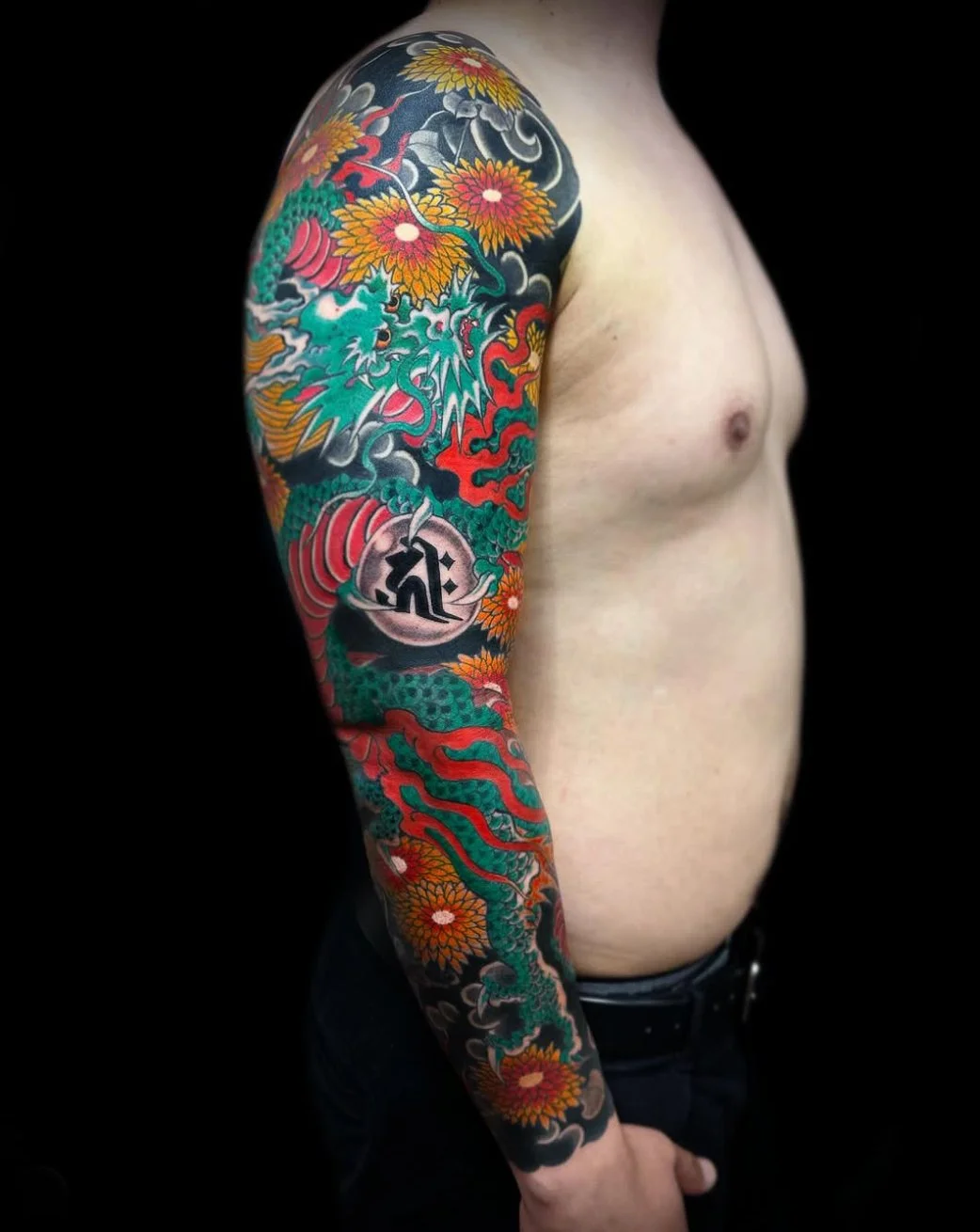 Close-up of a person's arm and shoulder with a colorful Japanese-style tattoo featuring a dragon, flowers, clouds, and other traditional elements.