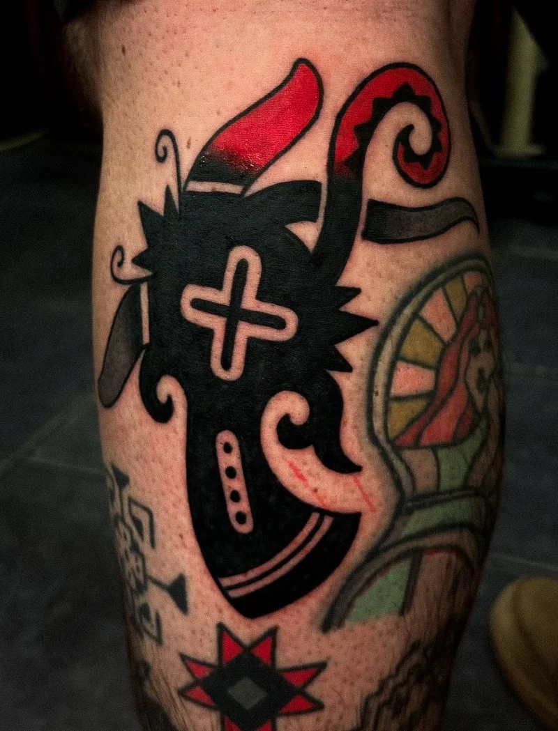 Tattoo of a stylized heart with a cross in the middle, surrounded by abstract shapes and colorful designs.