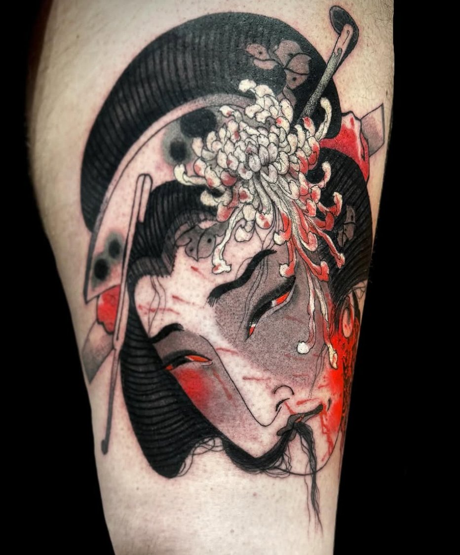 Tattoo of a geisha woman's face with traditional hair, red and black accents, holding a fan, with additional red, black, and gray elements surrounding her.