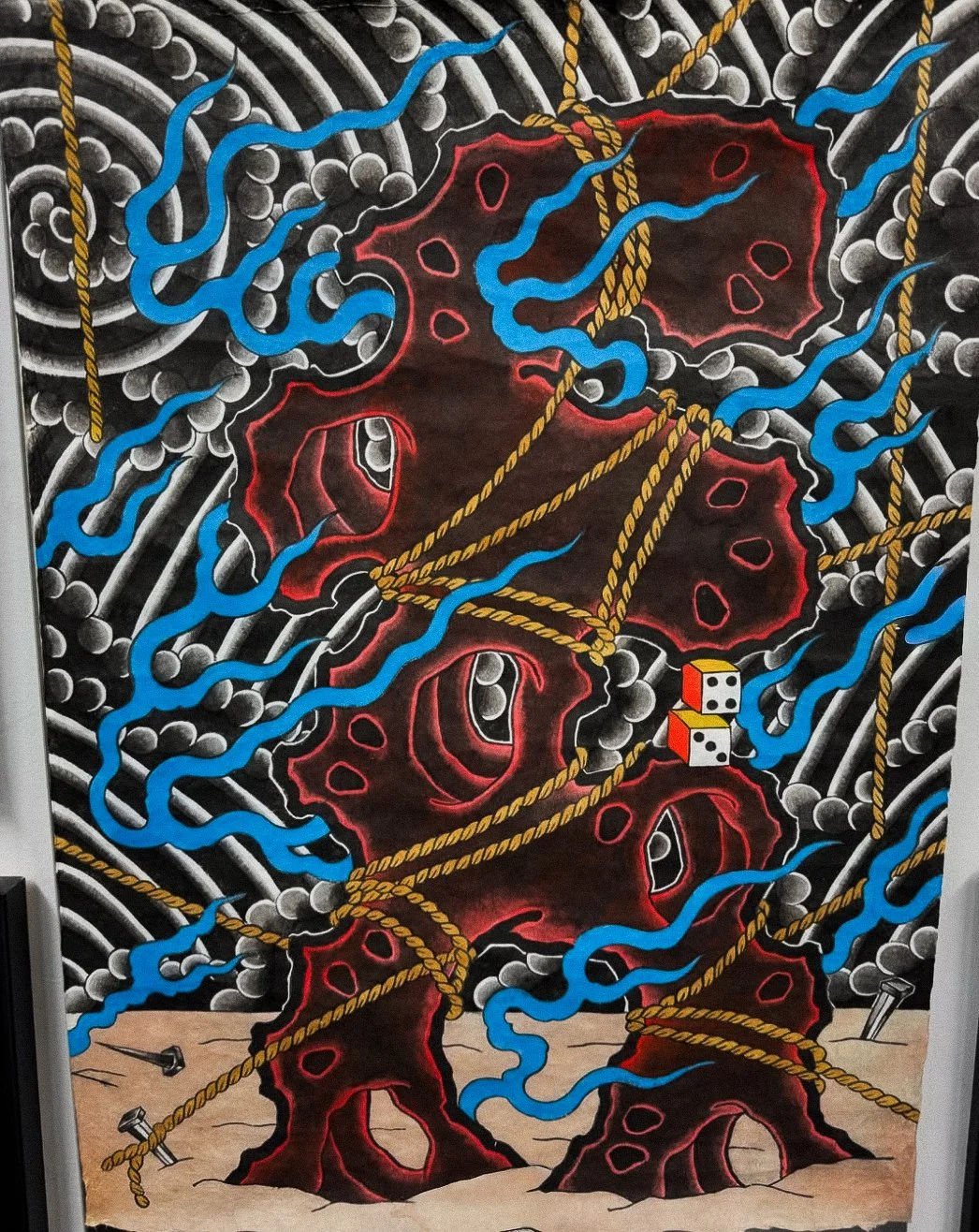 An abstract mural featuring a dark textured background with red and black organic shapes. Blue squiggly lines and yellow ropes intertwined, with dice floating near the ropes and nails on the ground.