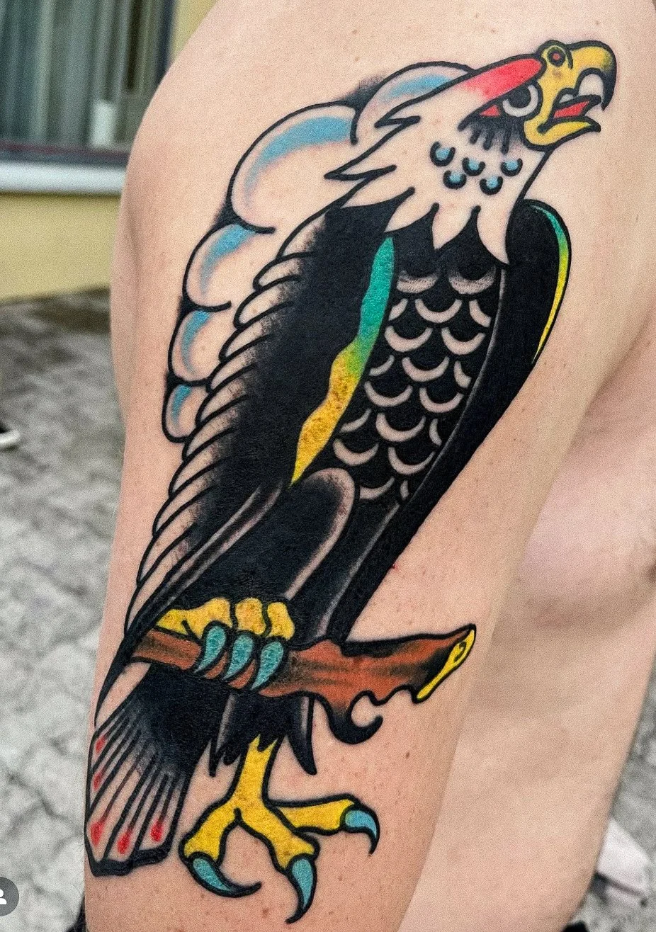 Tattoo of a stylized eagle with colorful accents on a person's upper arm.