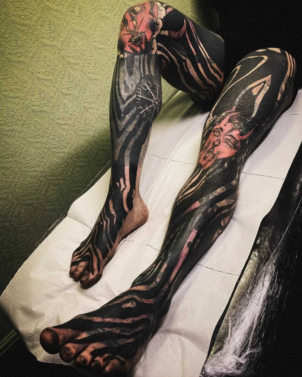 A person lying on a white surface with extensive black and pink tattoos covering both legs and arms.