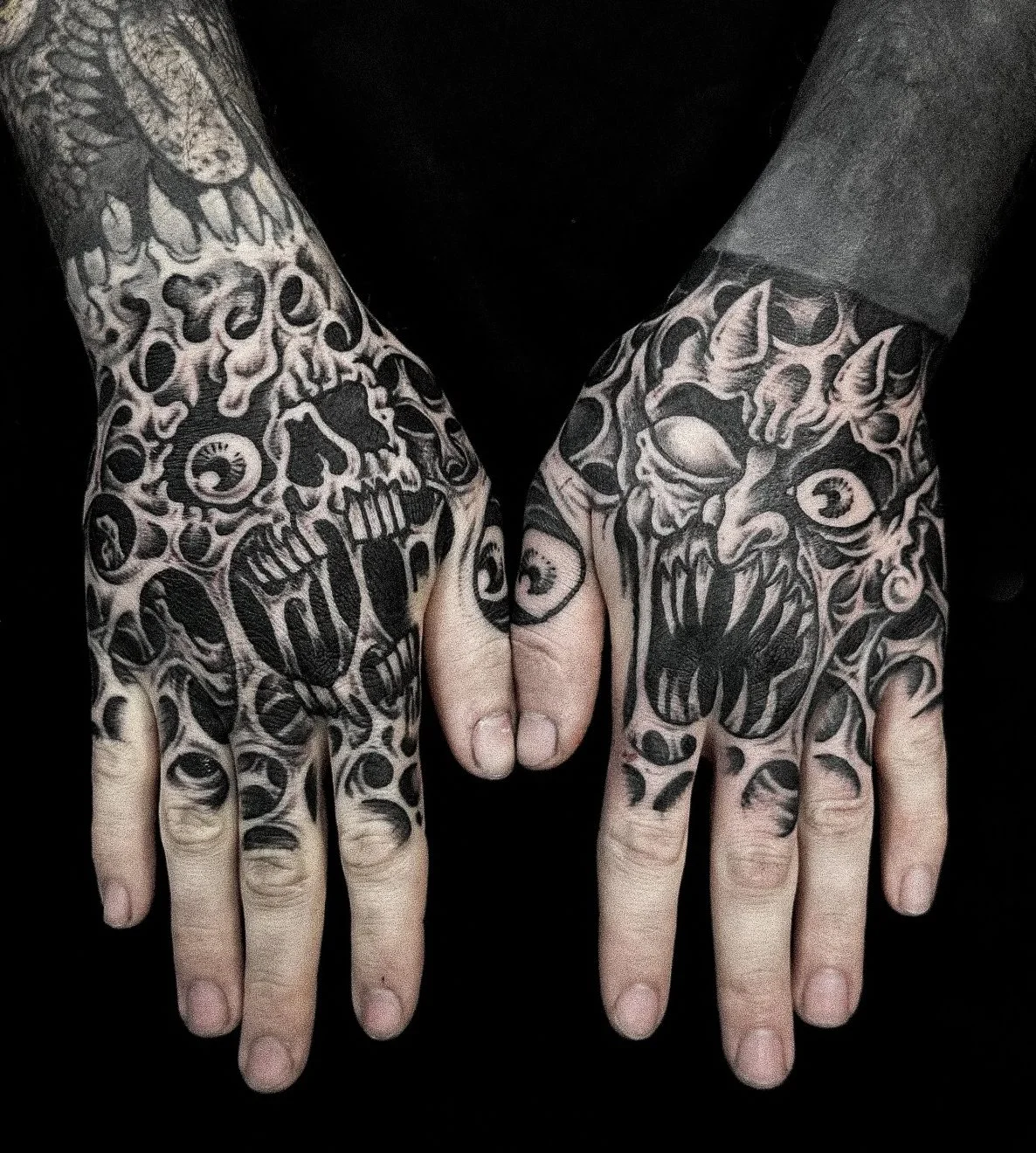 Two tattooed hands touching fists, with detailed black and gray tattoos featuring skulls, eyes, and abstract designs.