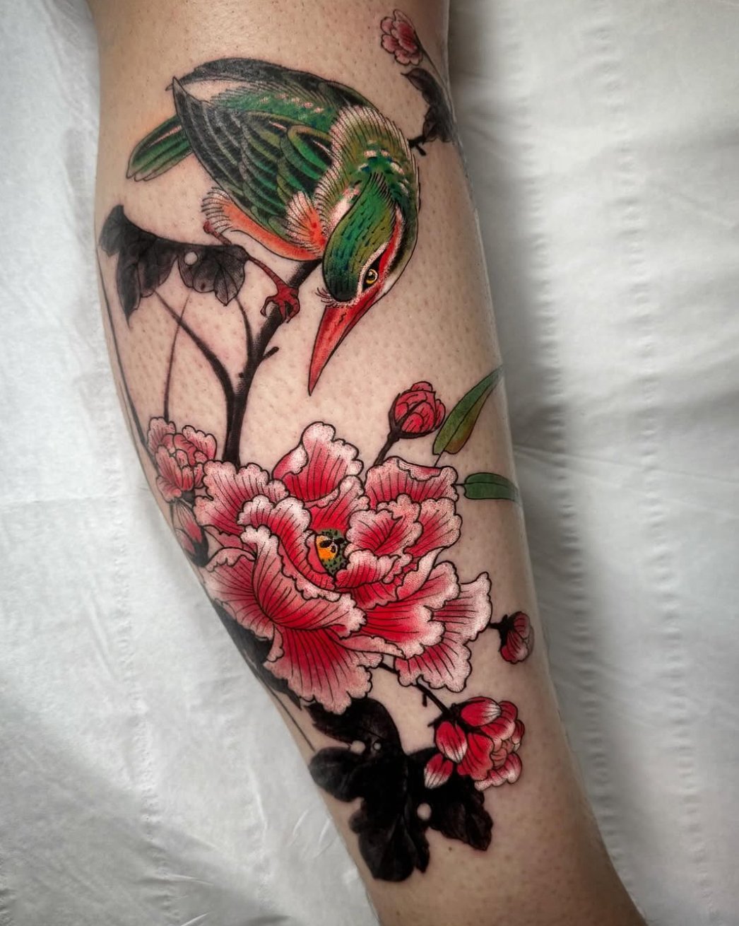 Colorful tattoo of a bird perched on a branch with pink flowers on a person's arm.