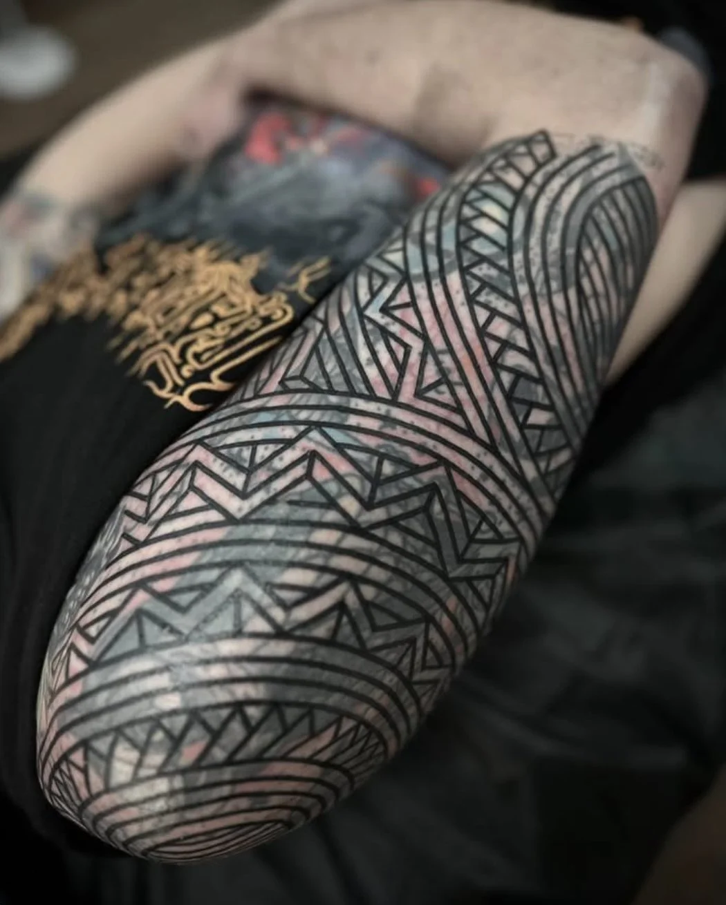 Close-up of a person's arm covered in tribal-style black ink tattoo with geometric patterns.