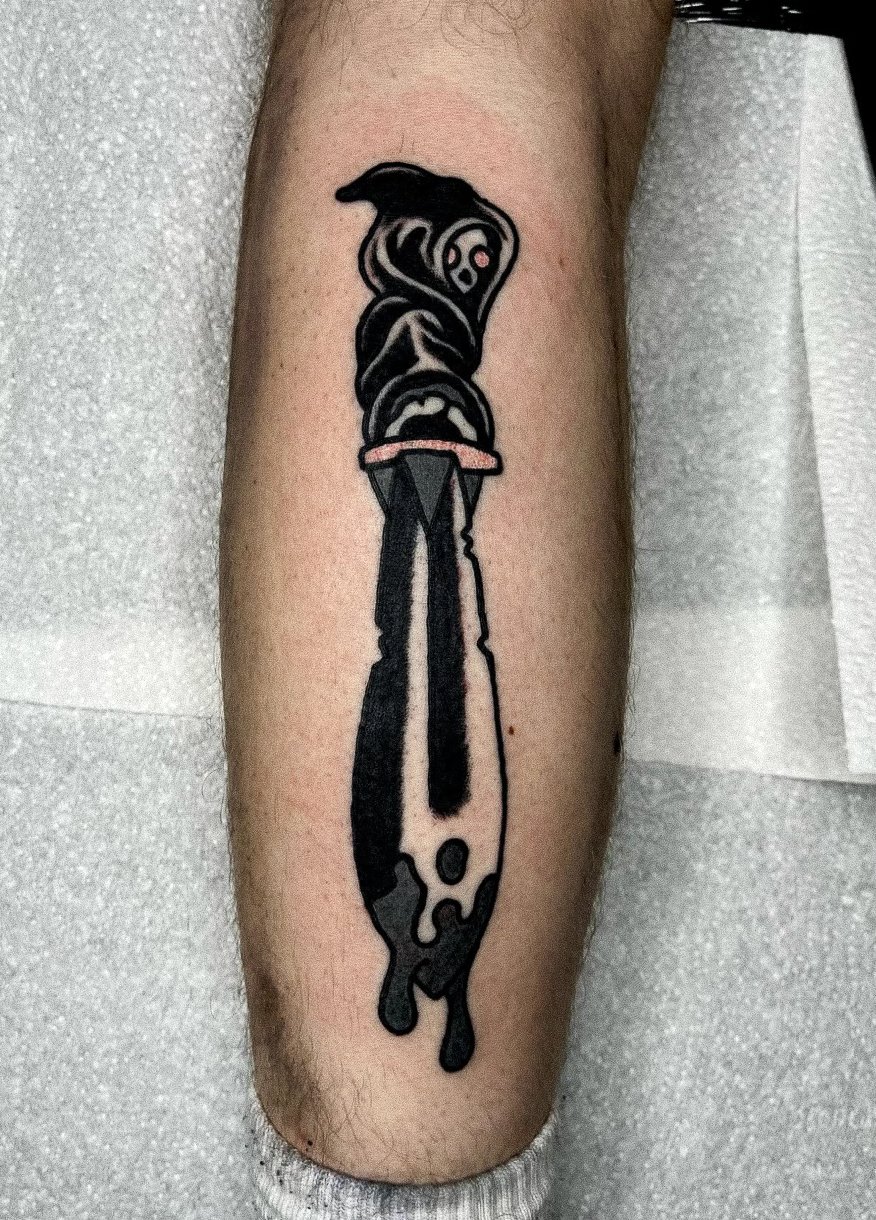 Tattoo of a stylized knife with black, gray, and pink ink on a person's lower leg.
