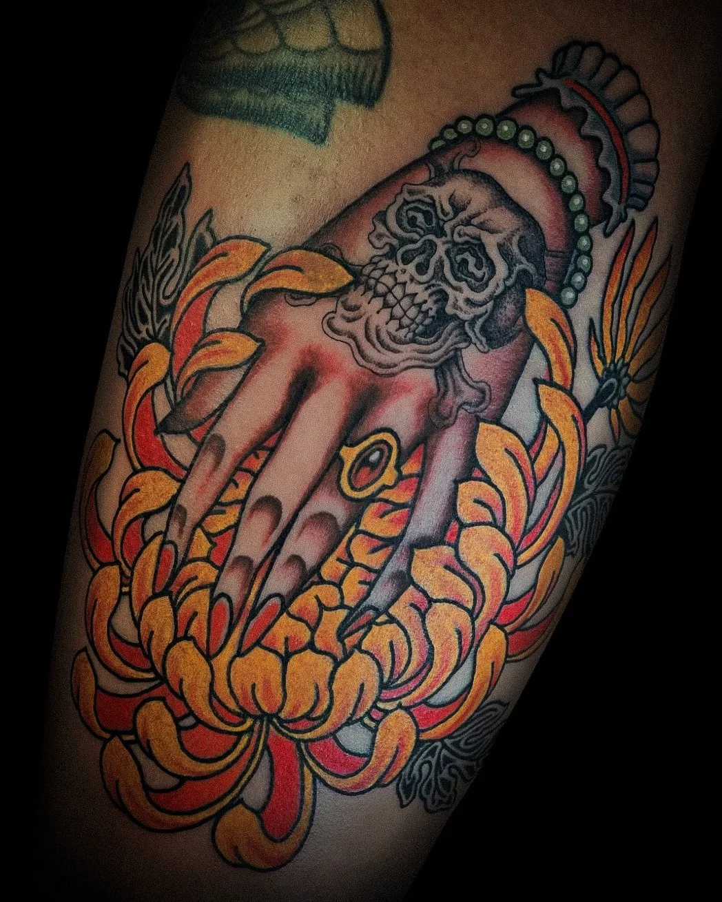 Tattoo of a human skull with a hand, surrounded by flames and decorative elements.