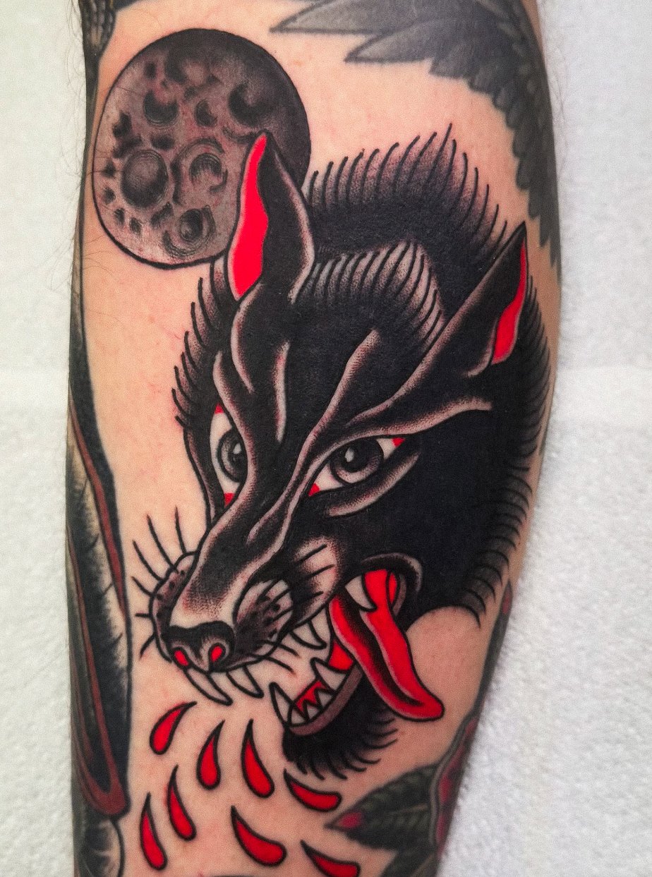 Tattoo of a black wolf with red eyes and tongue, bleeding red droplets, under a full moon with cratered surface.