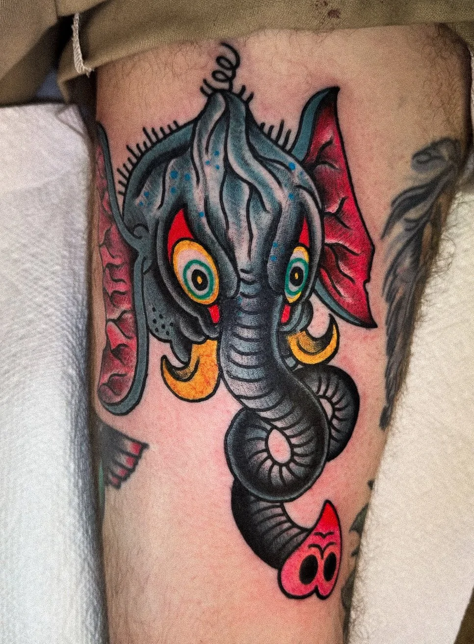 Tattoo of an abstract elephant with colorful eyes and earring on person's thigh