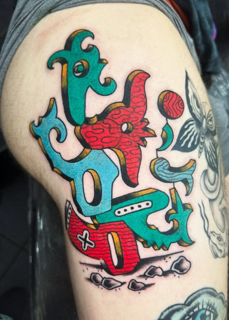 Colorful tattoo on person's arm with stylized text, a red dragon, a butterfly, a balloon, and clouds, in a comic or illustrative style.