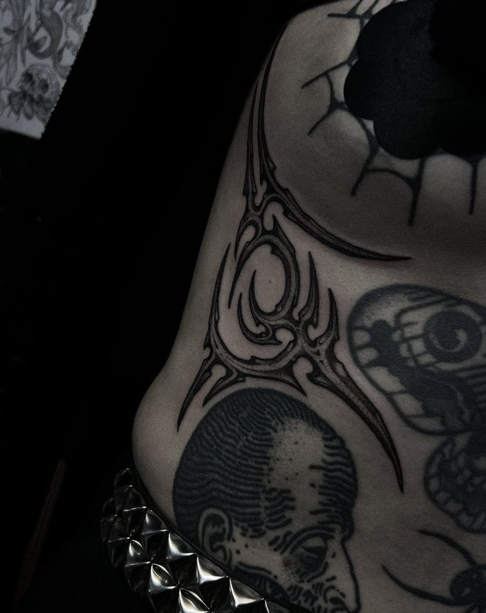 Close-up of tattoos on a person's skin, including a skull, a black circle with spikes, and tribal designs.