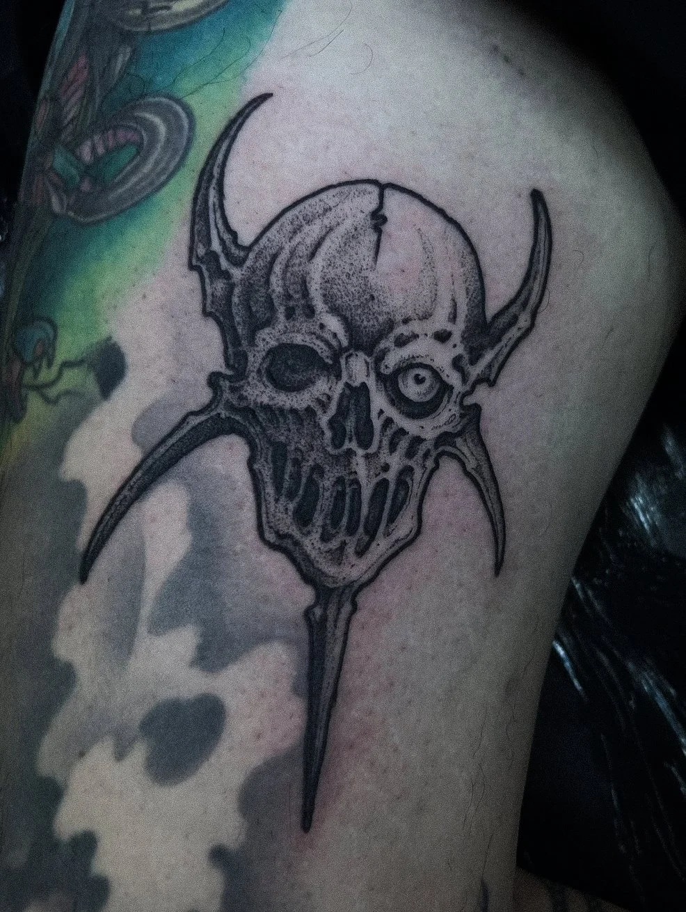 Black ink tattoo of a skull with horns and sharp teeth on a person's skin.