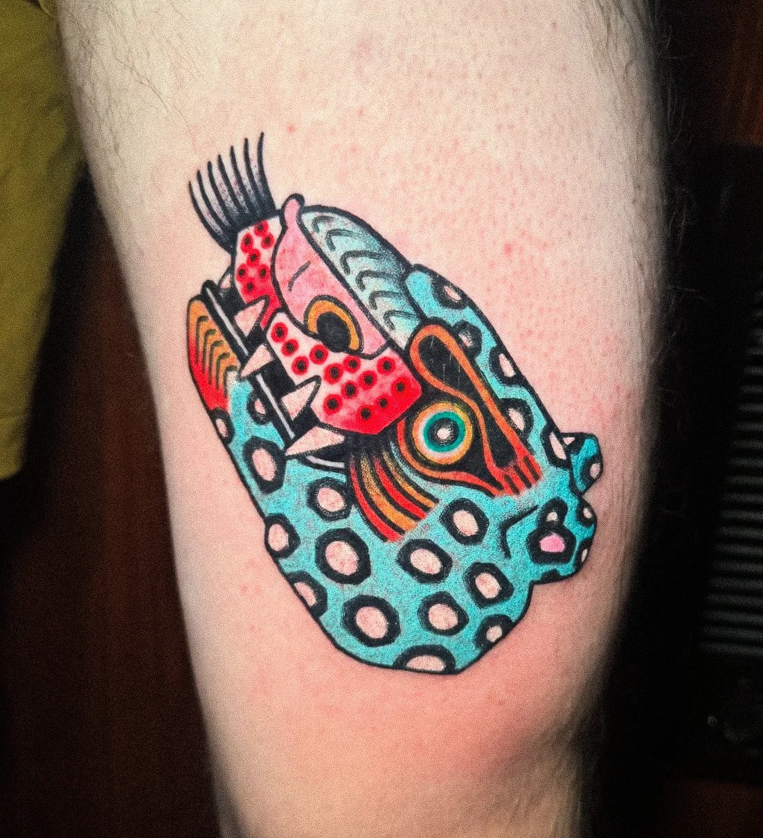 Colorful tattoo of a stylized snake coiled around a geometric shape, featuring bright colors and bold outlines.