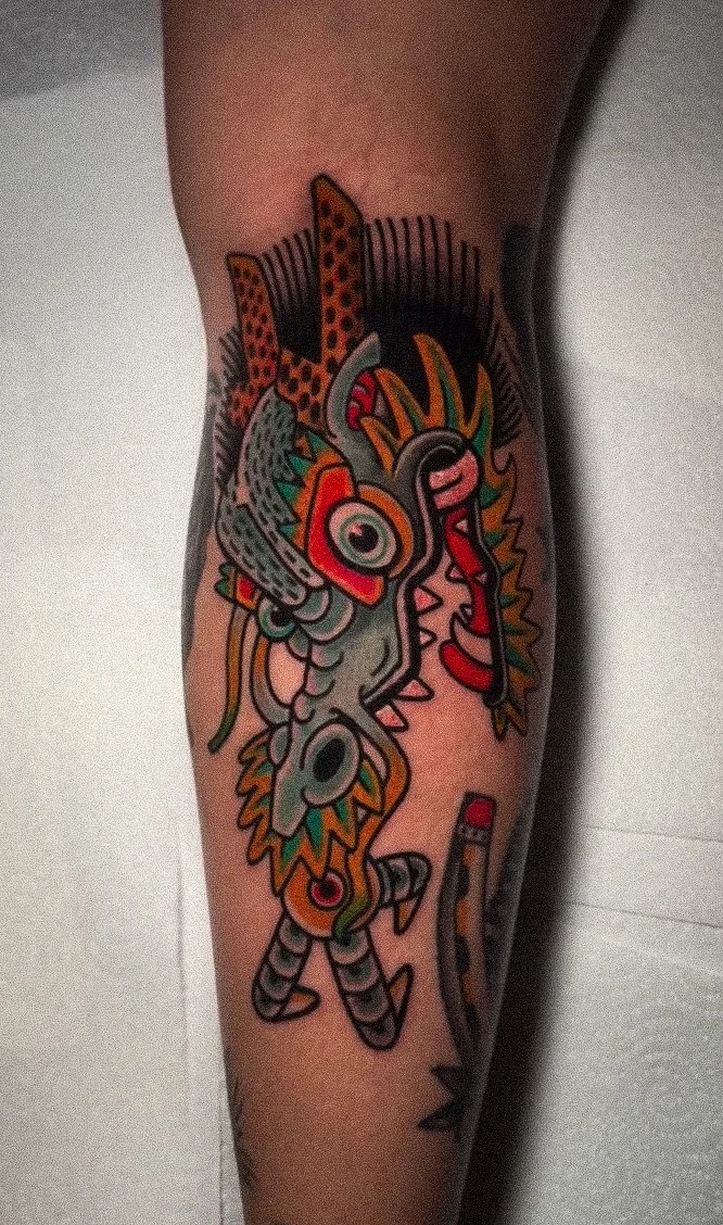 Colorful tattoo of a stylized dragon or mythical creature with various patterns and vibrant colors on a person's upper arm.