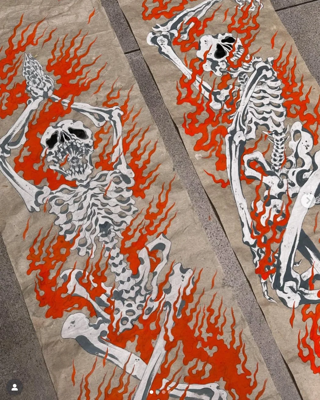 Two large skeleton illustrations with red flames surrounding them on brown paper sheets placed on a tiled floor.