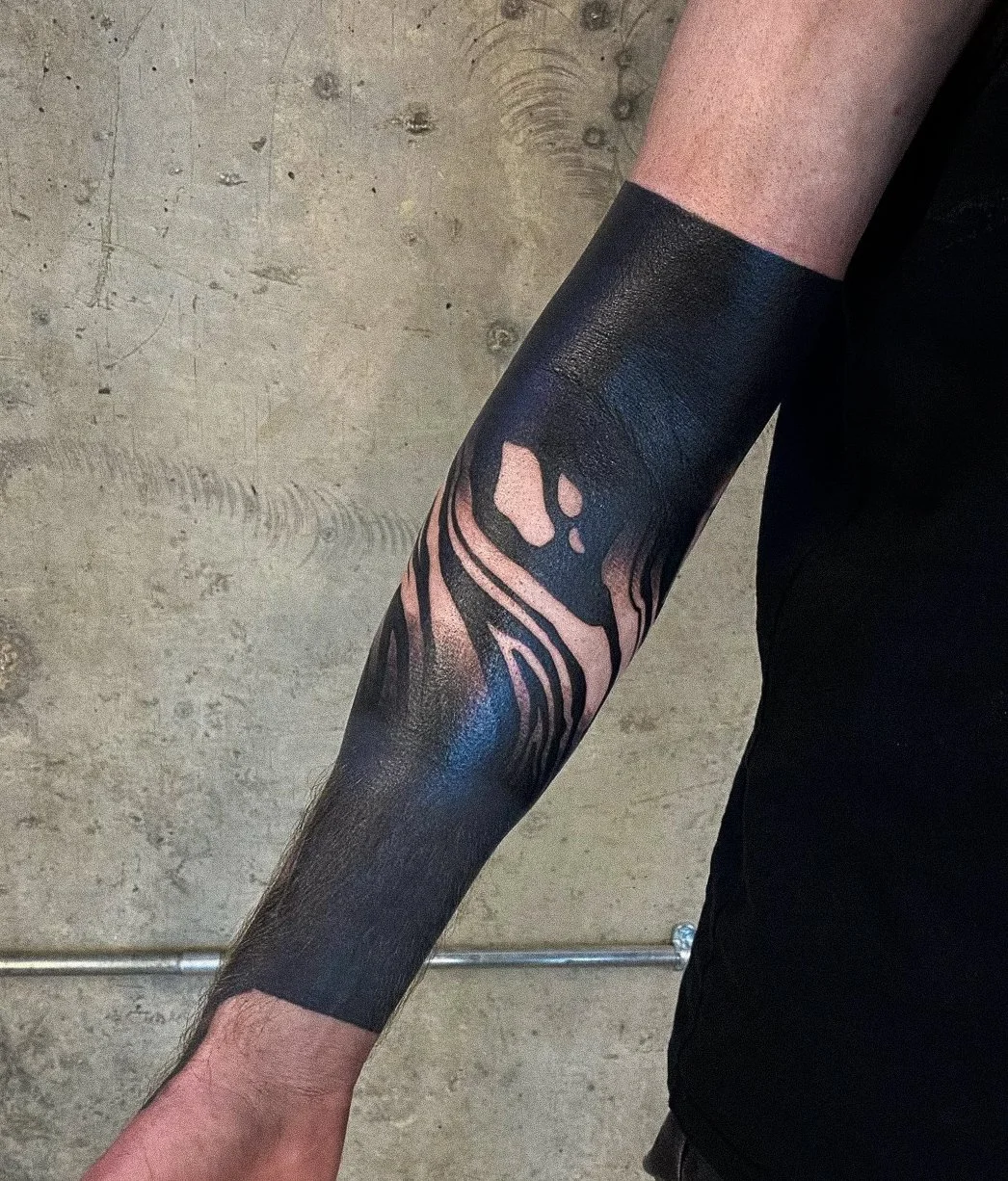 A person's arm with a black and pink zebra stripe tattoo on the forearm.