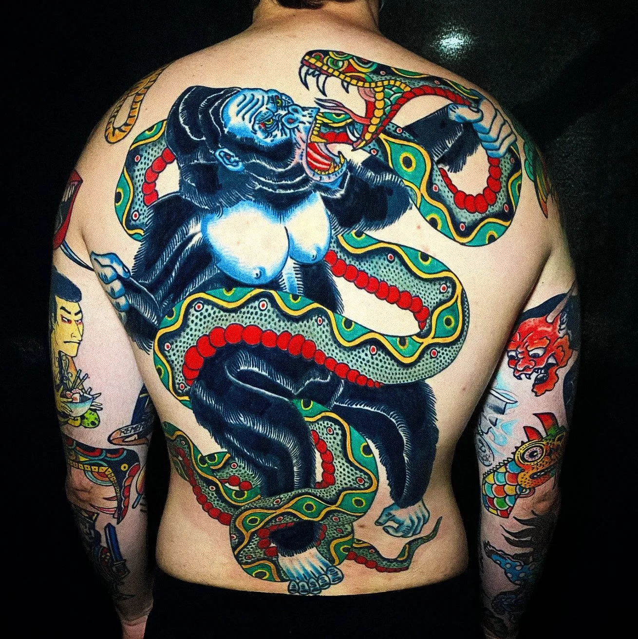 Tattoo of a blue tiger and a colorful dragon intertwined on a person's back, with additional tattoos on arms.