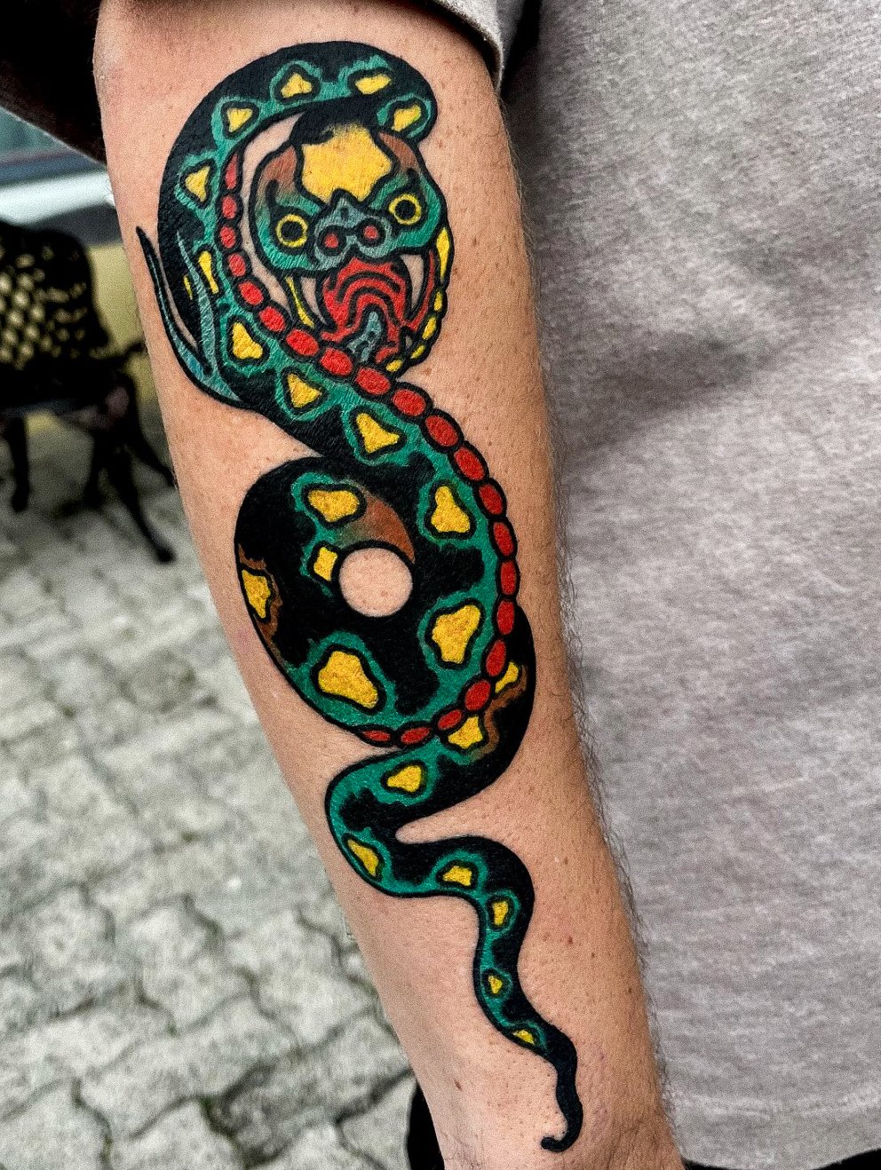 Colorful tattoo of a snake with a detailed, stylized face on a person's forearm.