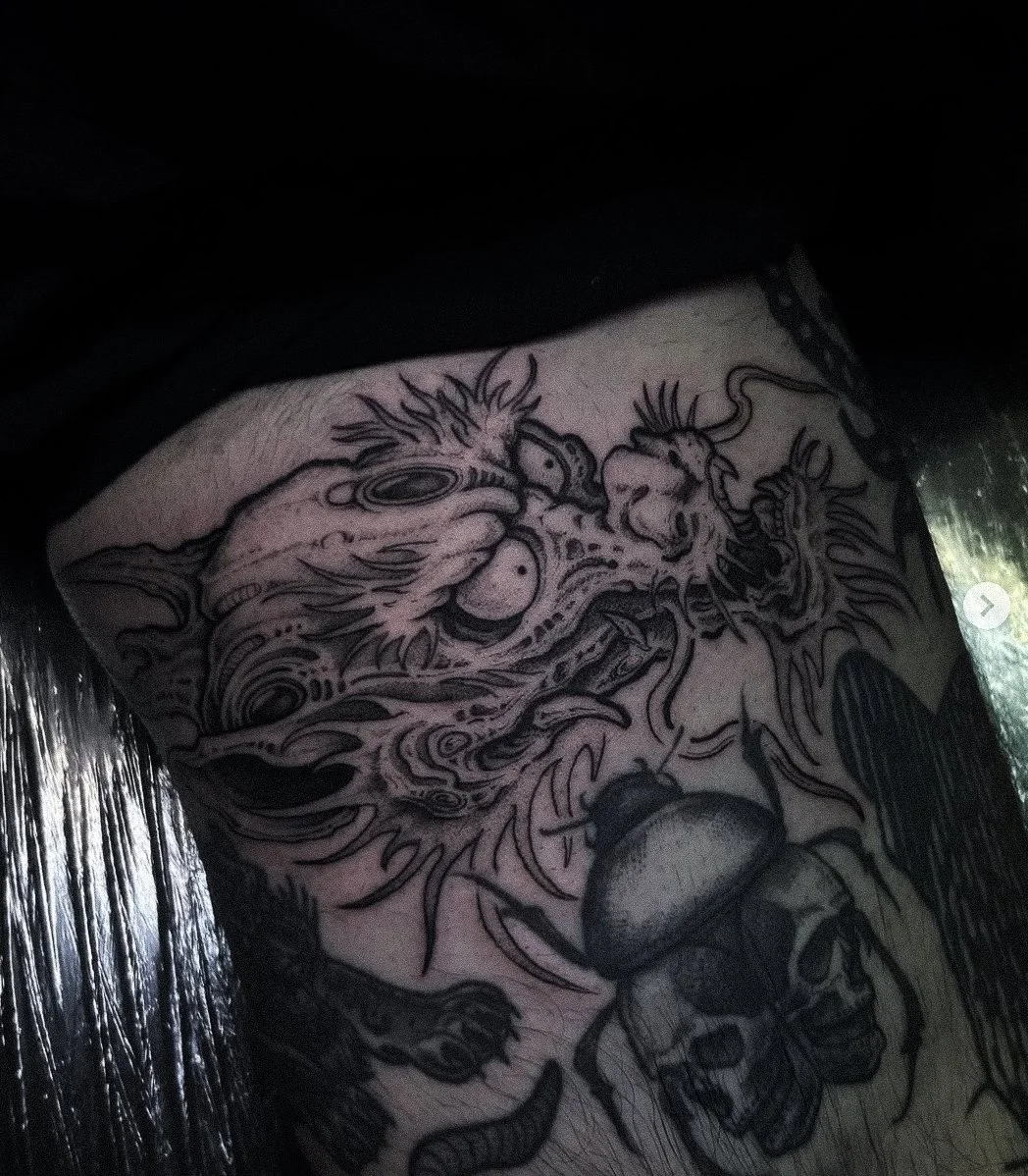 Close-up of a tattoo featuring a dragon and a skull with a mushroom on top.
