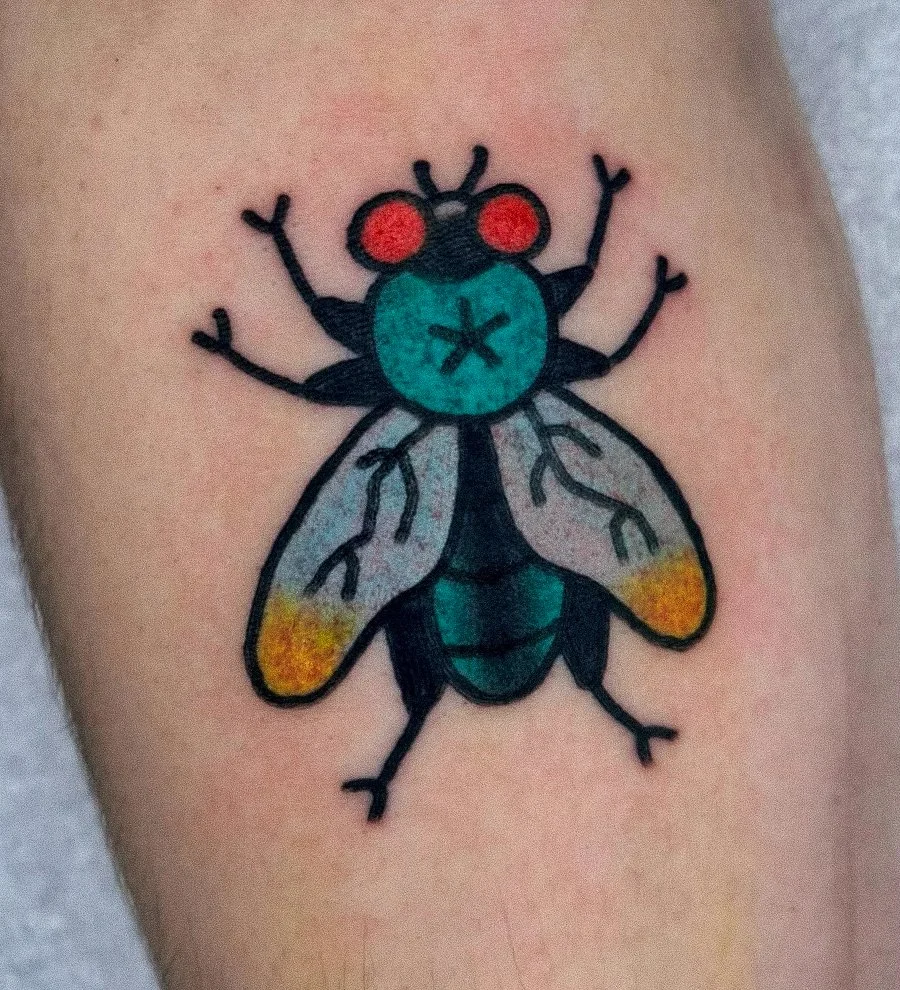 Colorful tattoo of a fly with red eyes, teal and yellow accents, and black outlines on skin.