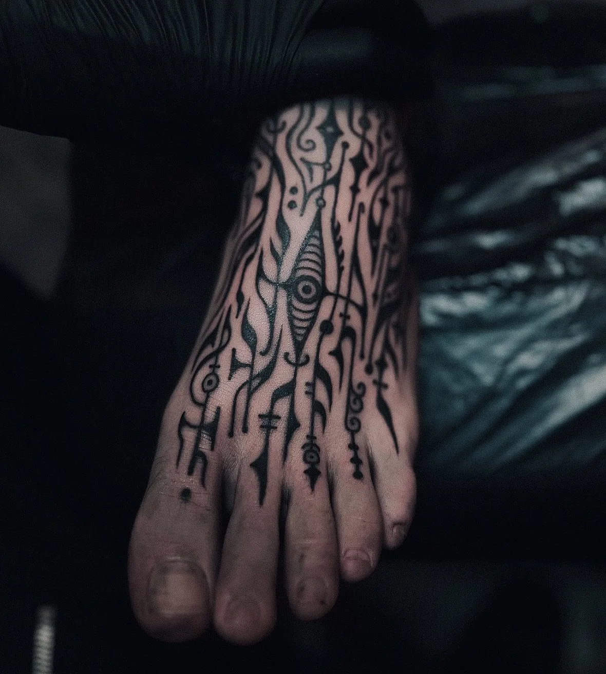 Black abstract tattoo on person's hand with various symbols and intricate line work.