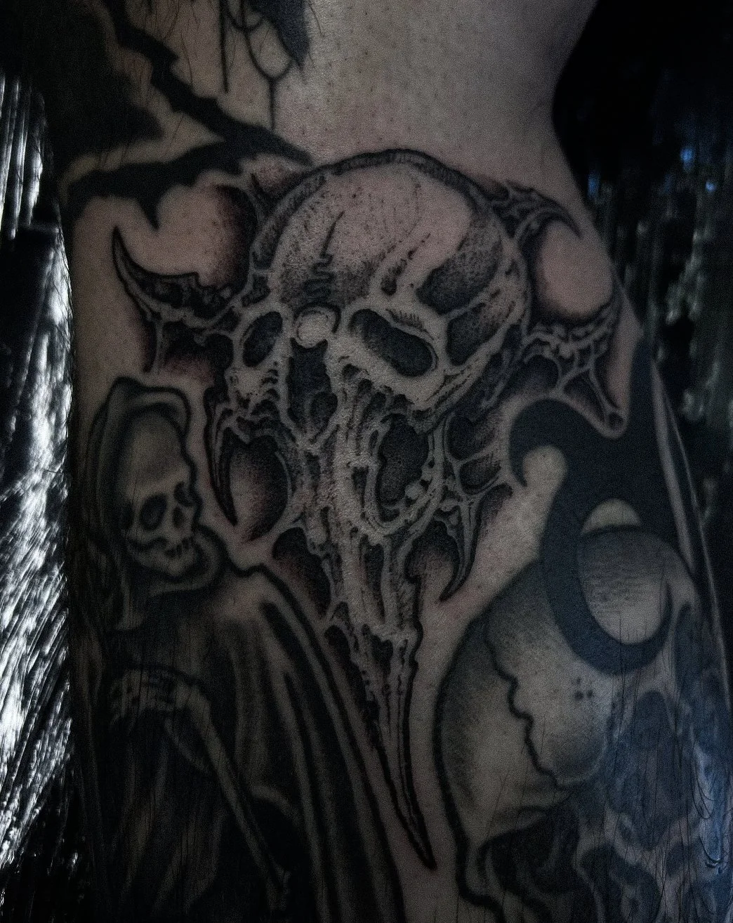 Black and gray tattoo of a skull with bat wings and a long, pointed snout.